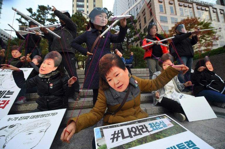 Protesters wearing masks of South Korean President Park Geun-Hye (front) and her confidante Choi Soon-Sil (back) perform before a candle-lit rally in central Seoul on October 29, 2016 to denounce Park over a high-profile corruption and influence-peddling scandal involving her close friend. South Korean prosecutors on October 29 raided the homes and offices of senior advisers to President Park Geun-Hye, as she struggled with a corruption and influence-peddling scandal involving a close family friend. / AFP PHOTO / JUNG YEON-JE