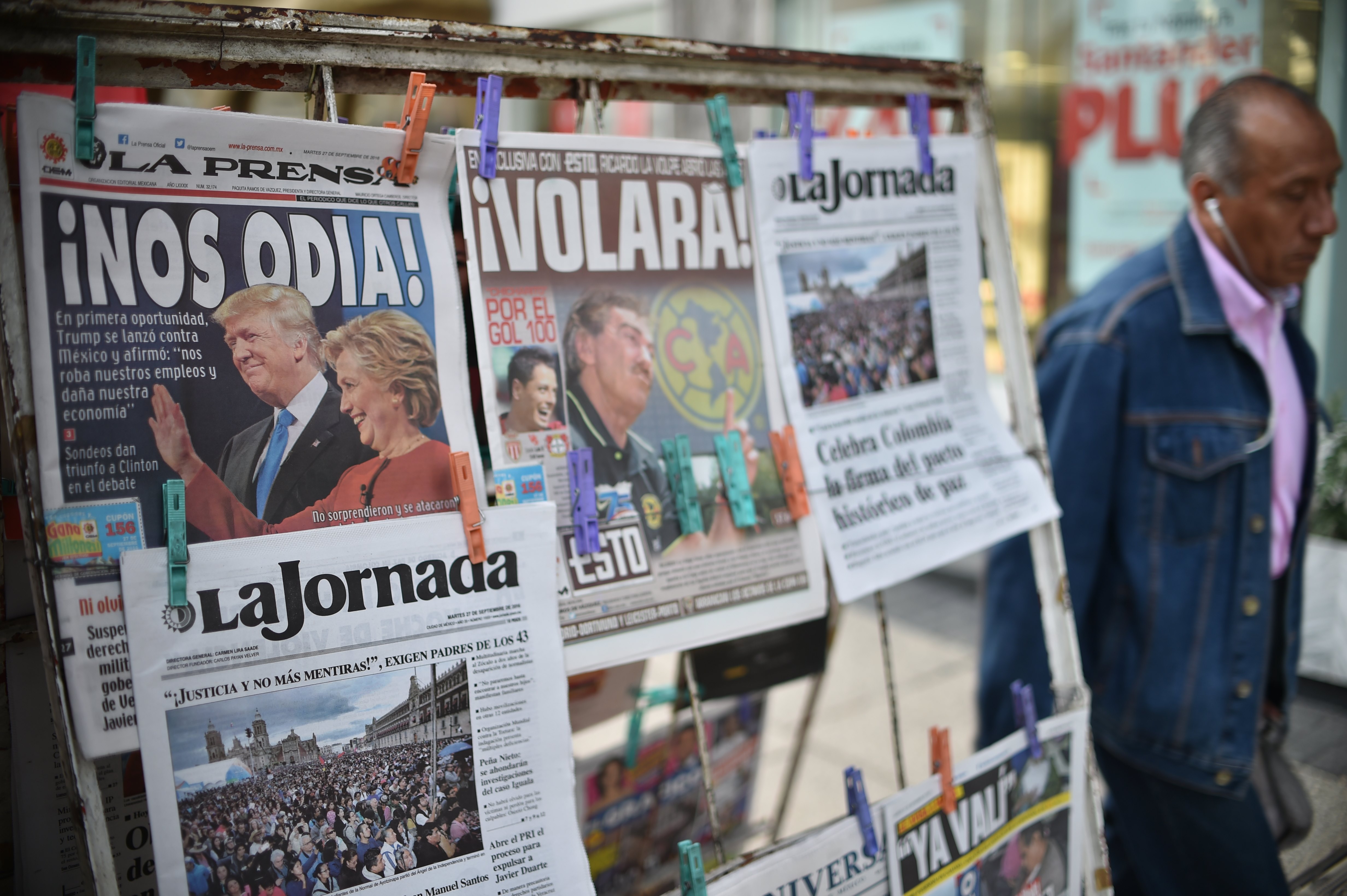 A man walks by a newsstand displaying front pages showing images of US presidential candidates debate and Colombia's peace agreement, in Mexico City on September 27, 2016. Hillary Clinton's upbeat performance in the first US presidential debate over Republican rival Donald Trump caused the Mexican peso to have a fiesta in Asian trading, rebounding off a record low, rocketing over two percent to 19.4367 against the dollar. / AFP PHOTO / YURI CORTEZ