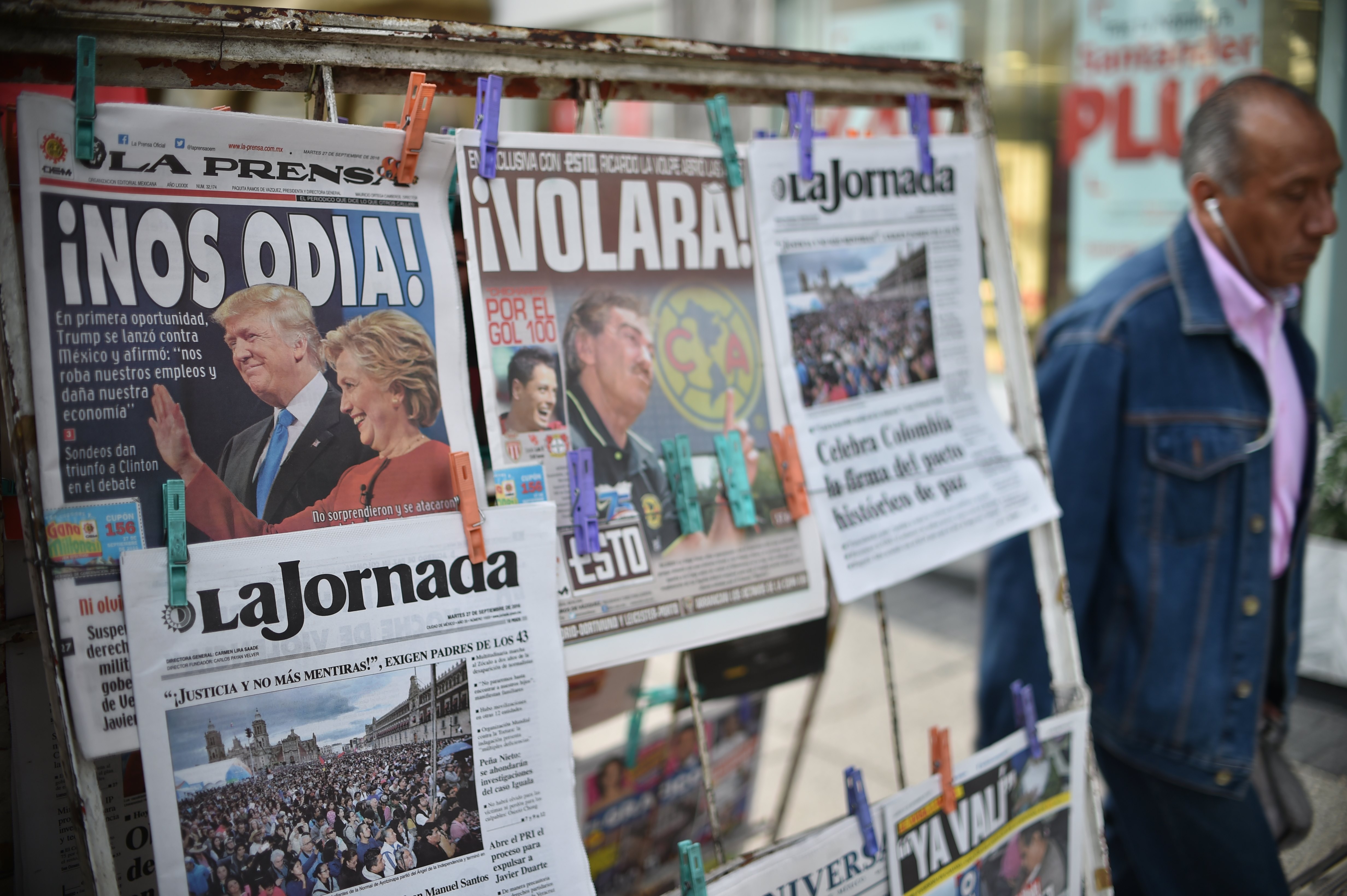 A man walks by a newsstand displaying front pages showing images of US presidential candidates debate and Colombia's peace agreement, in Mexico City on September 27, 2016.  Hillary Clinton's upbeat performance in the first US presidential debate over Republican rival Donald Trump caused the Mexican peso to have a fiesta in Asian trading, rebounding off a record low, rocketing over two percent to 19.4367 against the dollar.  / AFP PHOTO / YURI CORTEZ