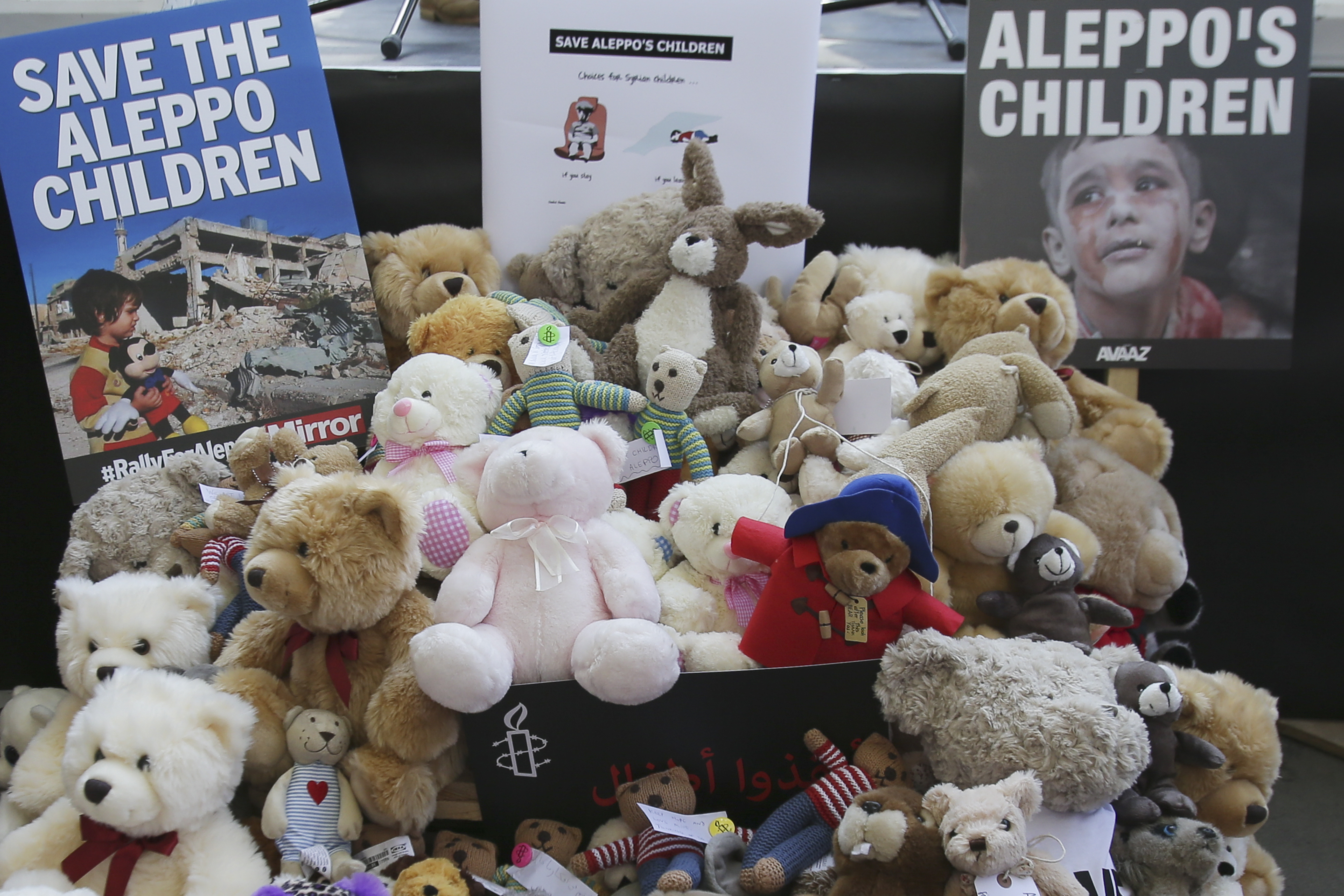 A pile of teddy bears nd placards are seen during a protest calling on the British government to take action to protect the children of the Syrian city of Aleppo outside Downing Street in central London on October 22, 2016.  Several campaign groups and charities including Avaaz and Amnesty International organised a rally outside Downing Street in London to call on the British government to set out a plan to protect Syrian children in the embattled Syrian city of Aleppo. Hundreds of wounded civilians were stranded in rebel-held areas of Syria's Aleppo on October 22 after the UN said security concerns had prevented evacuation convoys even as Russia extended a ceasefire into a third day. / AFP PHOTO / Daniel Leal-Olivas