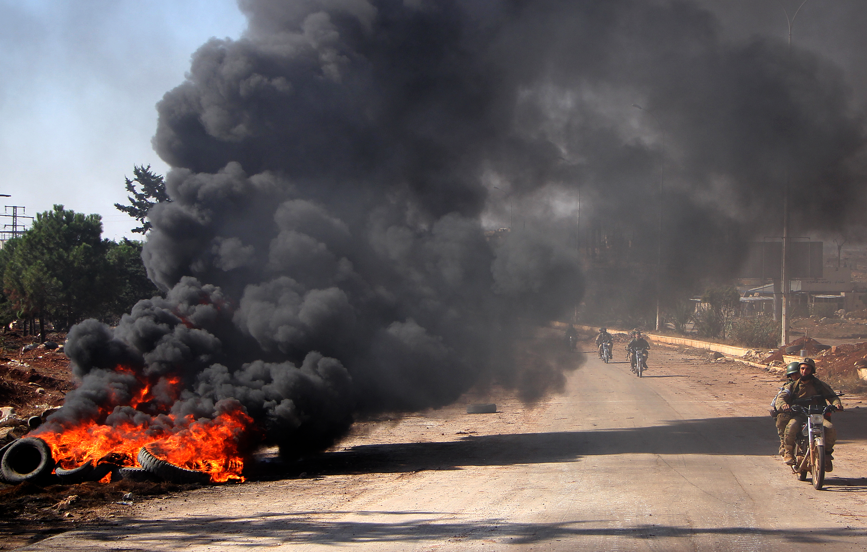 Rebel fighters from the Jaish al-Fatah (or Army of Conquest) brigades drive past burning tyres on November 3, 2016, at an entrance to Aleppo, in the southwestern frontline near the neighbourhood of Dahiyet al-Assad, during a rebel offensive to break a three-month siege of the opposition-held east of Syria's second city. Syrian rebels launched a new wave of car bombs and rockets on Aleppo's western districts, redoubling their efforts to break the government's three-month siege of the city. / AFP PHOTO / Omar haj kadour