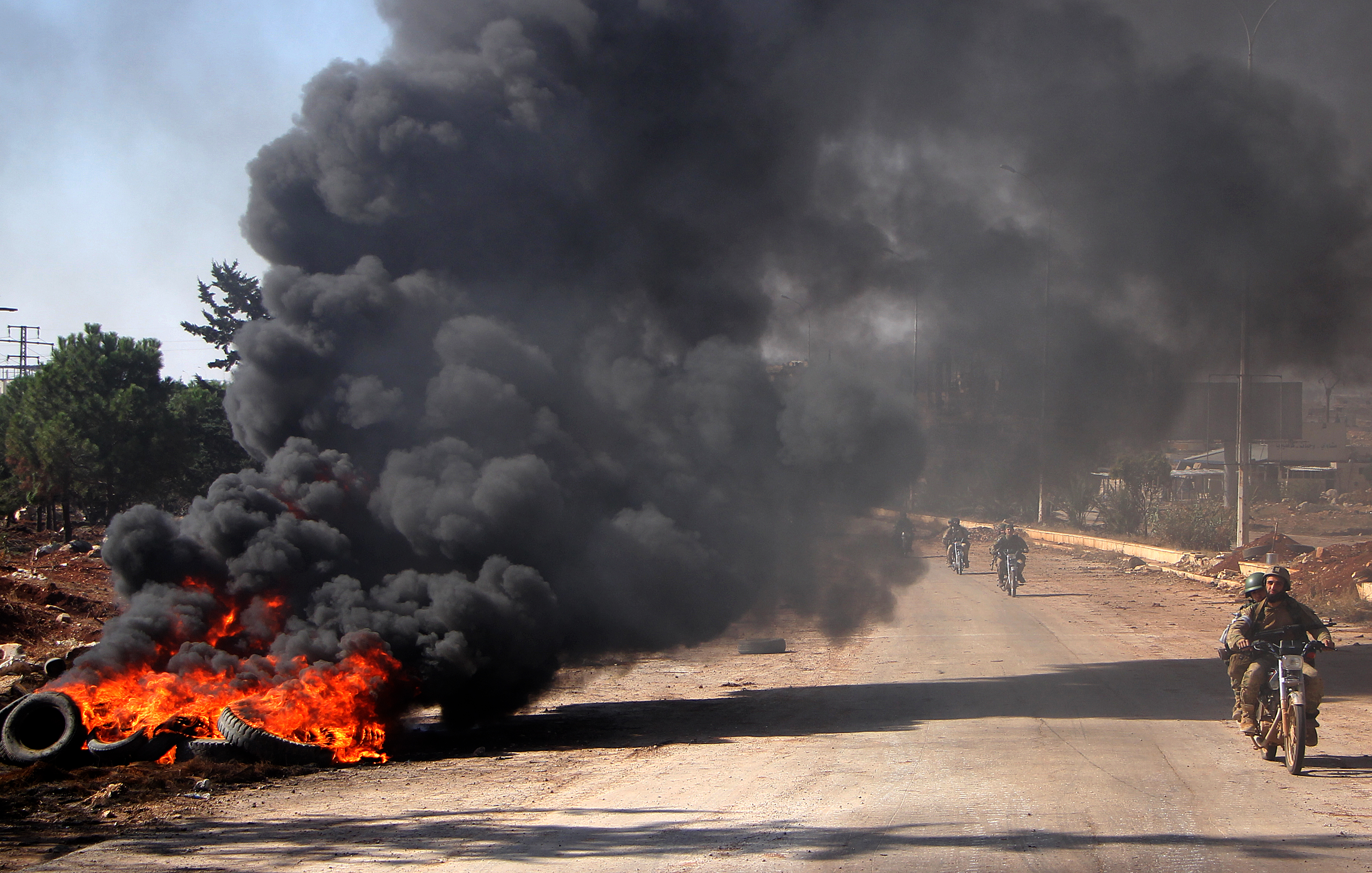 Rebel fighters from the Jaish al-Fatah (or Army of Conquest) brigades drive past burning tyres on November 3, 2016, at an entrance to Aleppo, in the southwestern frontline near the neighbourhood of Dahiyet al-Assad, during a rebel offensive to break a three-month siege of the opposition-held east of Syria's second city.  Syrian rebels launched a new wave of car bombs and rockets on Aleppo's western districts, redoubling their efforts to break the government's three-month siege of the city. / AFP PHOTO / Omar haj kadour