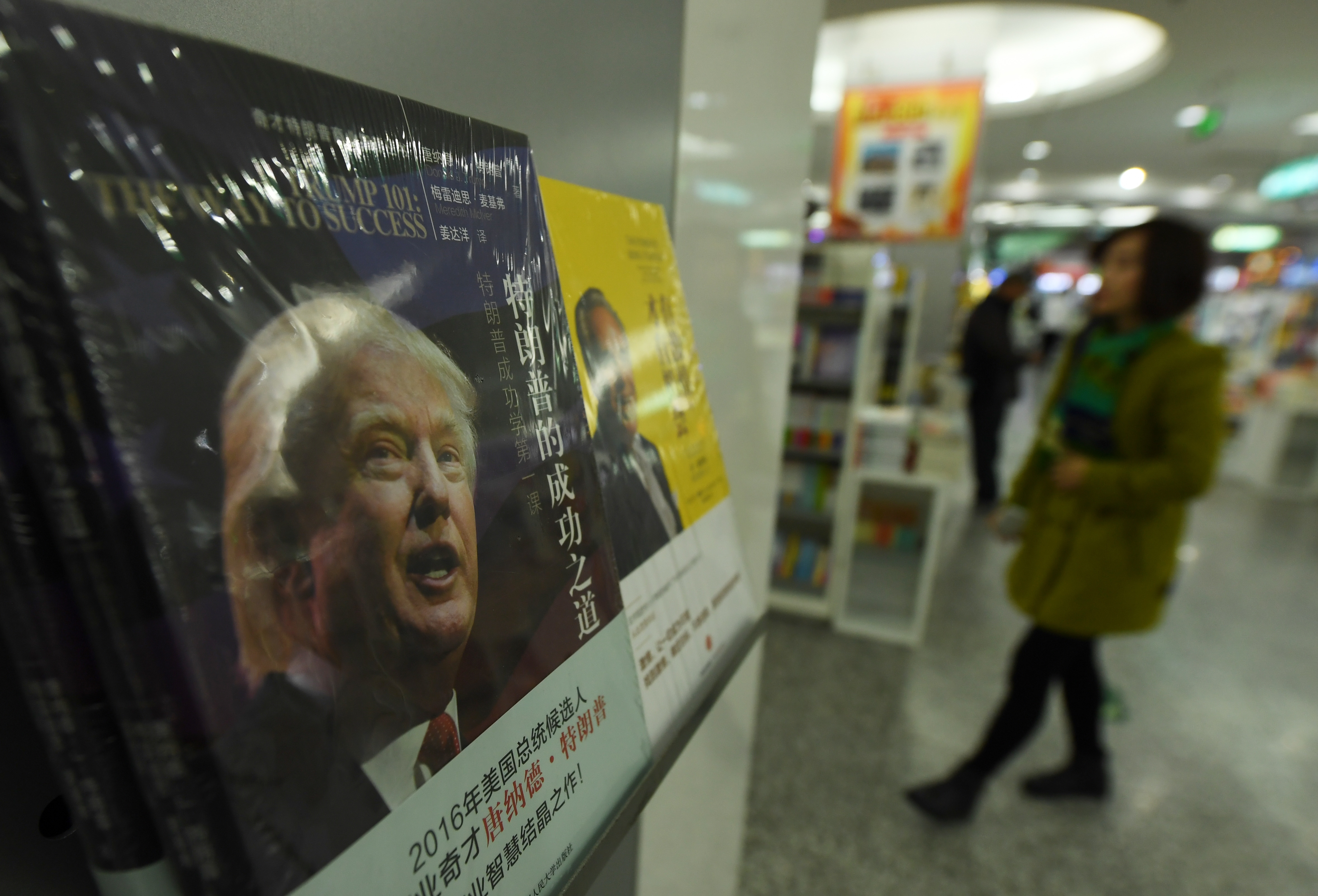 A woman walks past a book about US presidential candidate Donald Trump in the business section of a book store in Beijing on November 7, 2016. No matter who triumphs, the US election has been a big win for China's national propaganda machine, which has gleefully catalogued the seemingly endless parade of skeletons marching out of America's political closet. / AFP PHOTO / GREG BAKER