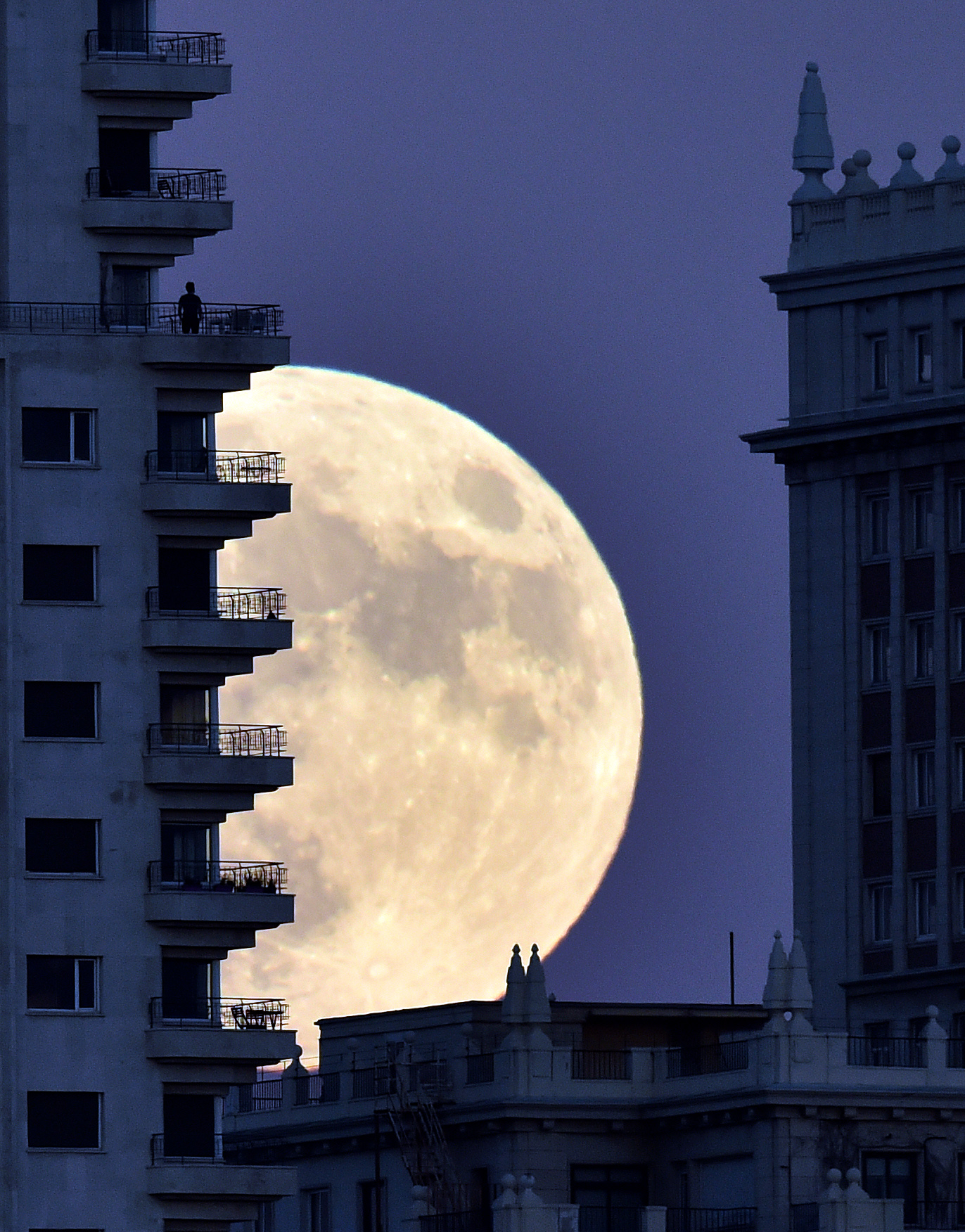 A man stands on a balcony of a building of Madrid as the moon rises in background, on November 13, 2016, on the eve of a "supermoon". On November 14, 2016, the moon will orbit closer to the earth than at any time since 1948, named a 'supermoon', it is defined by a Full or New moon coinciding with the moon's closest approach to the Earth. / AFP PHOTO / GERARD JULIEN