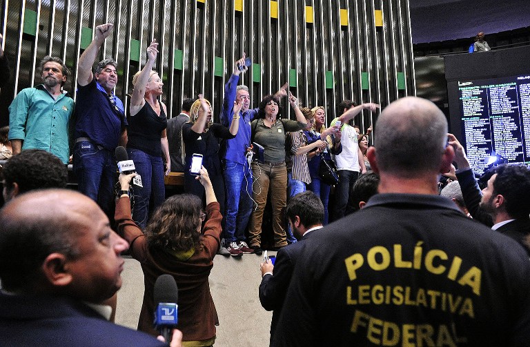 Demonstrators in favor of a military intervention in Brazil invade the lower house plenary session in Brasilia on November 16, 2016. Dozens of rightwing protesters burst into Brazil's legislative chamber on Wednesday to demand a military coup. / AFP PHOTO / Agencia Camara / LUIS MACEDO