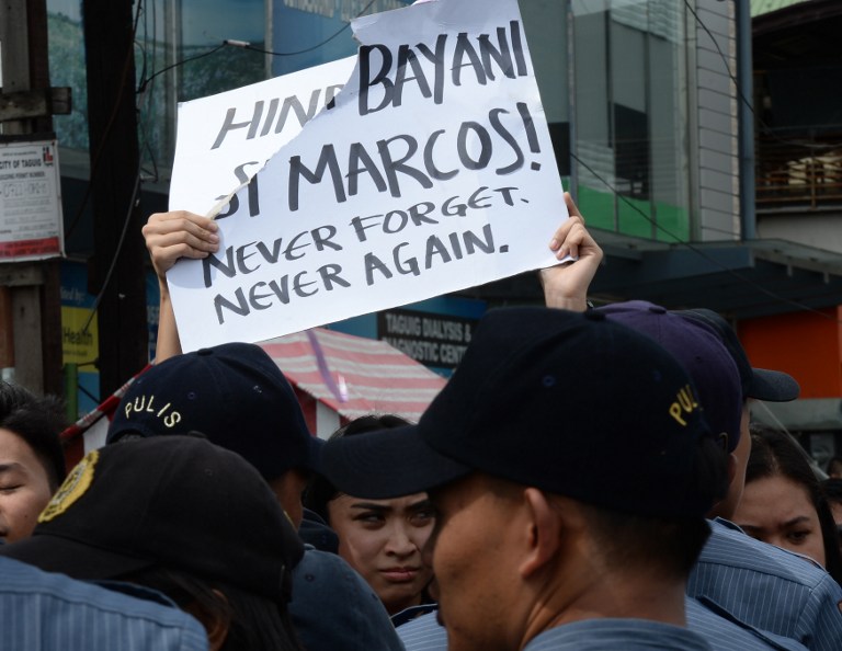 Anti-Marcos protestors are blocked by policemen near the entrance of the heroes' cemetery while the late dictator Ferdinand Marcos was being given a heroe's burial in Manila on November 18, 2016. Ex-Philippine dictator Ferdinand Marcos was buried at the national heroe's cemetery in a secretive ceremony, outraging opponents who said it whitewashed his brutal rule and tainted the famous 1986 "People Power" revolution that toppled him. / AFP PHOTO / TED ALJIBE