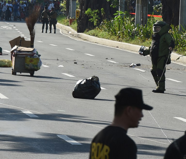 A member of police bomb disposal unit (R) holding a water bomb disruptor, walks towards the site where a suspicious package was found, for detonation along Roxas boulevard near the US embassy in Manila on November 28, 2016. According to press reports quoting the police, the suspicious package was found inside a box along a with a cell phone and another electronic device, which the police successfully detonated. / AFP PHOTO / TED ALJIBE