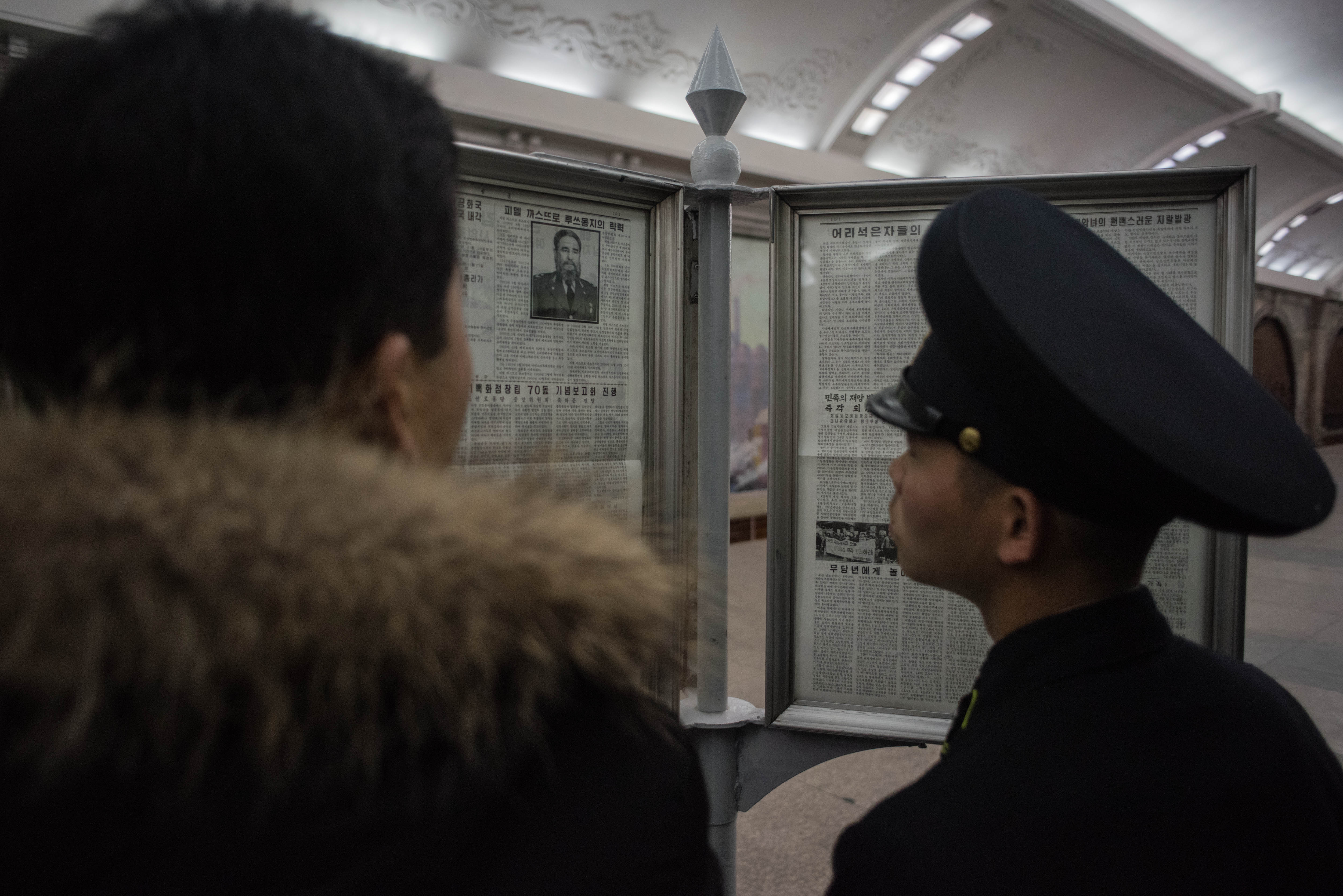 A guard reads a newspaper article announcing the death of former Cuban leader Fidel Castro, at a subway station in Pyongyang on November 28, 2016. / AFP PHOTO / Ed JONES