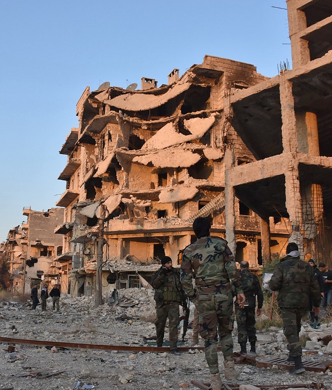 Syrian pro-government forces walk past destroyed buildings in Aleppo's Bustan al-Basha neighbourhood on November 28, 2016, during their assault to retake the entire northern city from rebel fighters. Government forces have retaken a third of rebel-held territory in Aleppo, forcing nearly 10,000 civilians to flee as they pressed their offensive to retake Syria's second city. In a major breakthrough in the push to retake the whole city, regime forces captured six rebel-held districts of eastern Aleppo over the weekend, including Masaken Hanano, the biggest of those in eastern Aleppo. / AFP PHOTO / GEORGE OURFALIAN