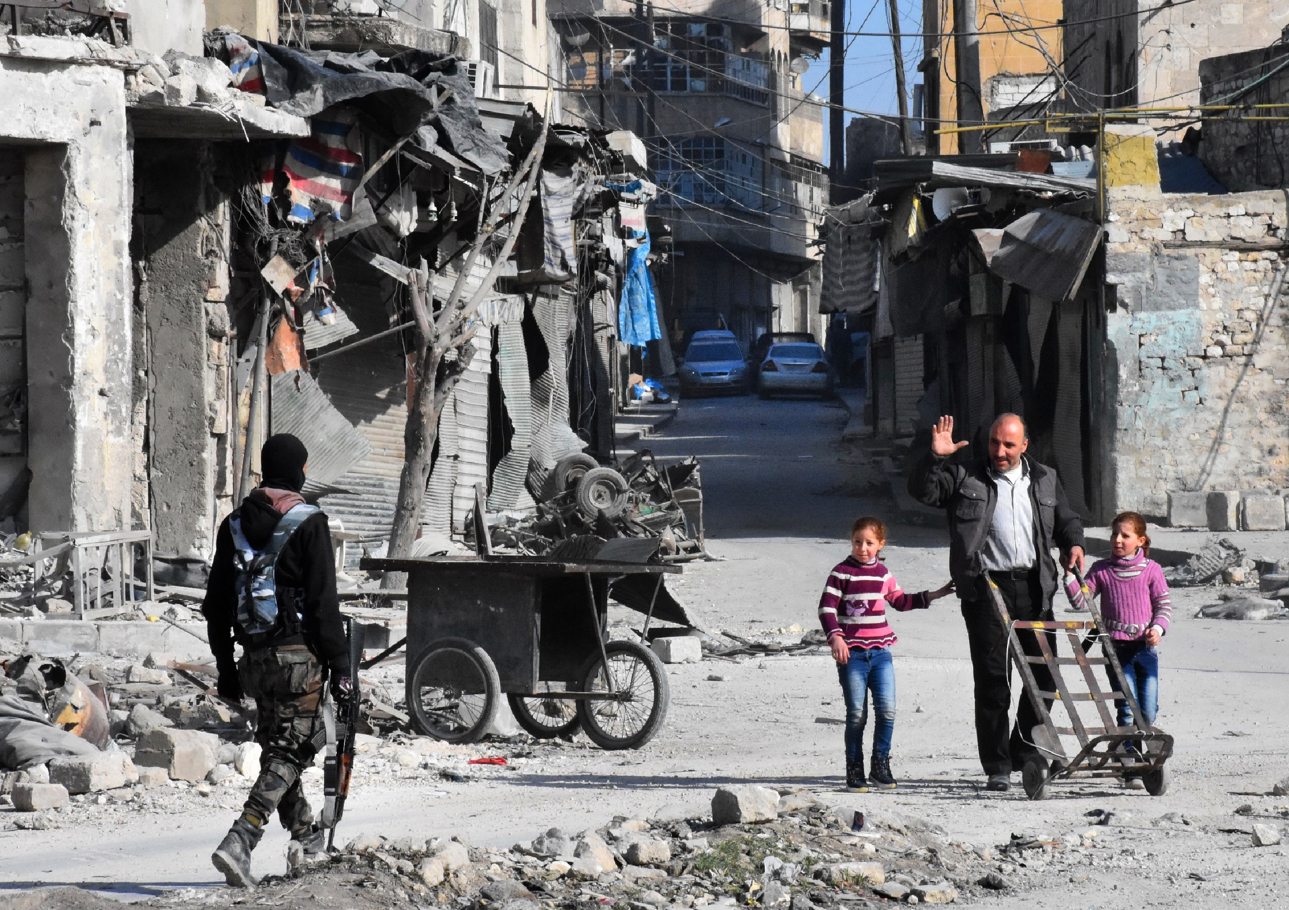 A man waves to a member of the Syrian pro-government forces patrolling a street in the newly retaken Bab al-Hadid neighbourhood in Aleppo's Old City on December 8, 2016. President Bashar al-Assad said victory for his forces in Aleppo would be a "huge step" in ending Syria's war, as government troops battled to retake more rebel ground. Regime forces have retaken about 80 percent of former rebel territory in Aleppo since launching an all-out offensive three weeks ago to recapture Syria's second city. / AFP PHOTO / GEORGE OURFALIAN