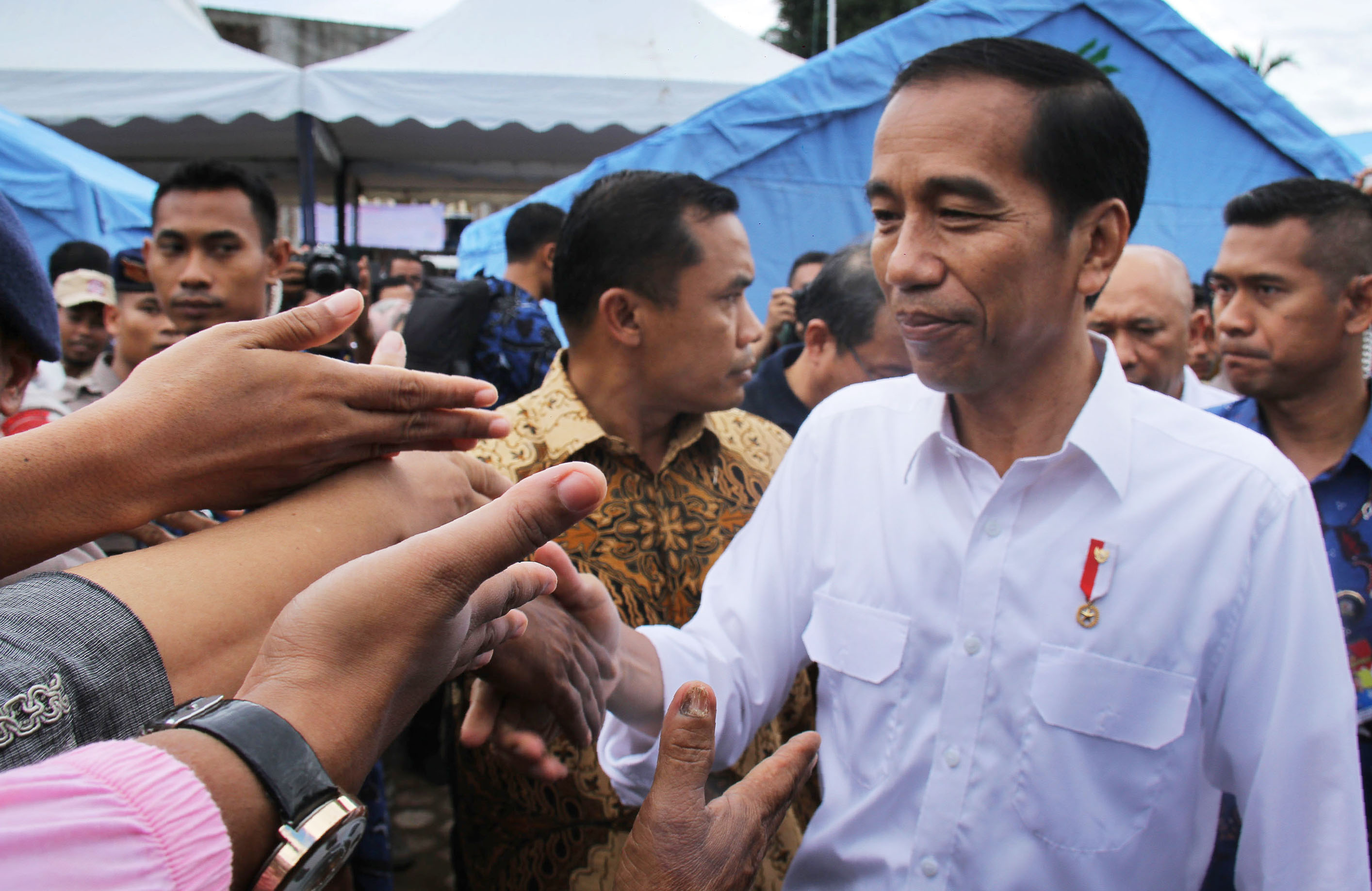 Indonesian President Joko Widodo (R) shakes hands with quake survivors at one of temporary shelter in Pidie Jaya, Aceh province, on December 9, 2016 during his two-day visit.  Widodo pledged to help the people of Aceh rebuild as he toured areas worst-hit by a devastating earthquake that killed more than 100 people and left thousands homeless. / AFP PHOTO / GATHA GINTING