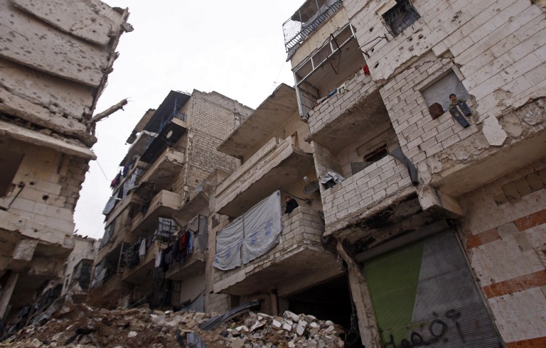 Residents in a government-held part of Aleppo's Salaheddin neighbourhood look out from the balconies of their damaged houses at the road on which the convoy evacuating civilians and rebel fighters from the last rebel-held neighbourhood in the northern Syrian city were supposed to pass on December 16, 2016. The Syrian government suspended the evacuation of civilians and fighters from the last rebel-held parts of Aleppo on Friday, leaving thousands of people trapped and uncertain of their fate. / AFP PHOTO / Youssef KARWASHAN