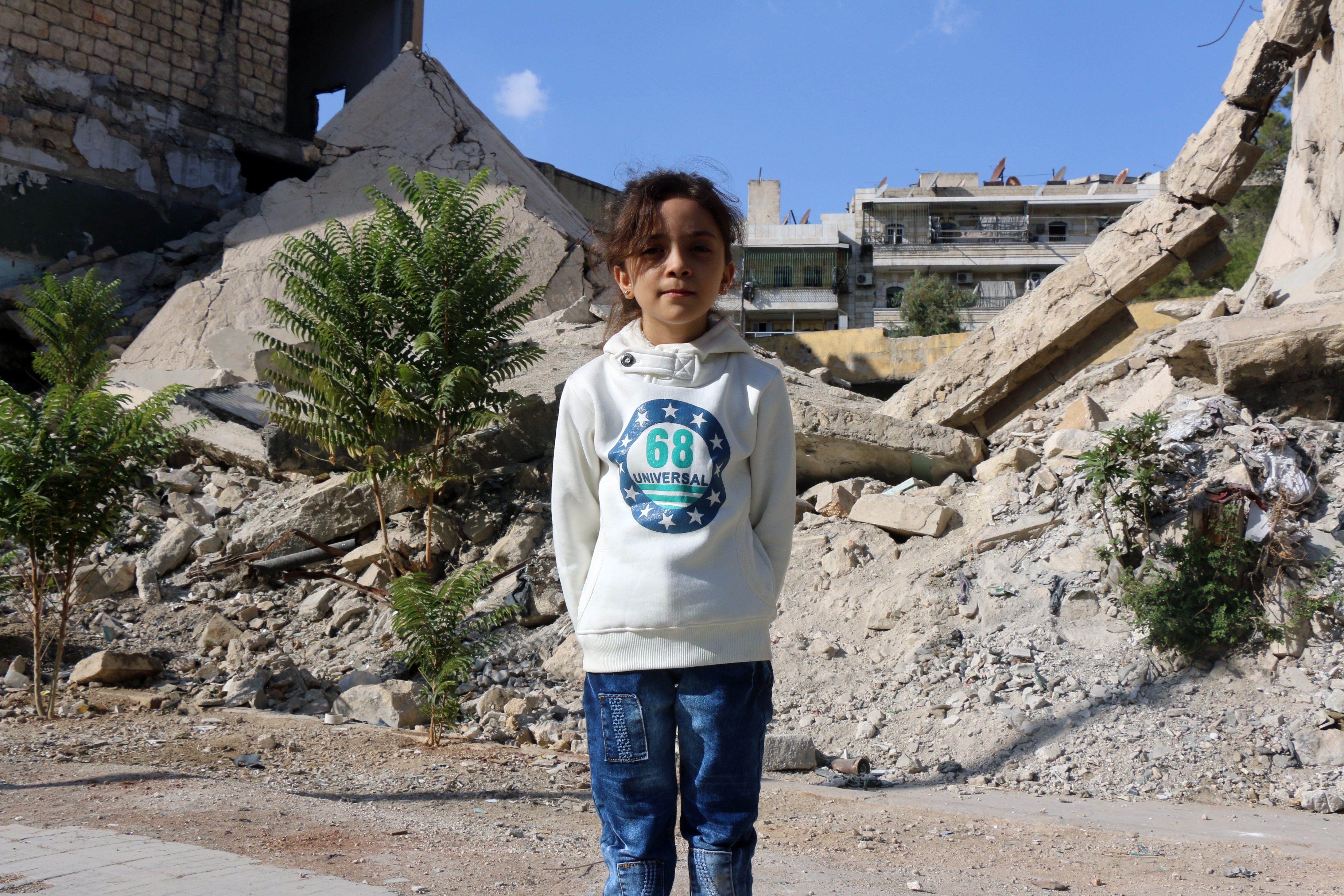 Syrian Bana al-Abed, who with the help of her mother had been posting heartrending tweets in English on life in the besieged eastern districts of Syria's Aleppo, poses for a picture amid the rubble of a destroyed building in east Aleppo on October 10, 2016. The seven-year-old Syrian girl whose Twitter account from Aleppo gained international attention has fled her home amid heavy fighting, but she and her family are safe for now, her father said on December 6, 2016. / AFP PHOTO / THAER MOHAMMED