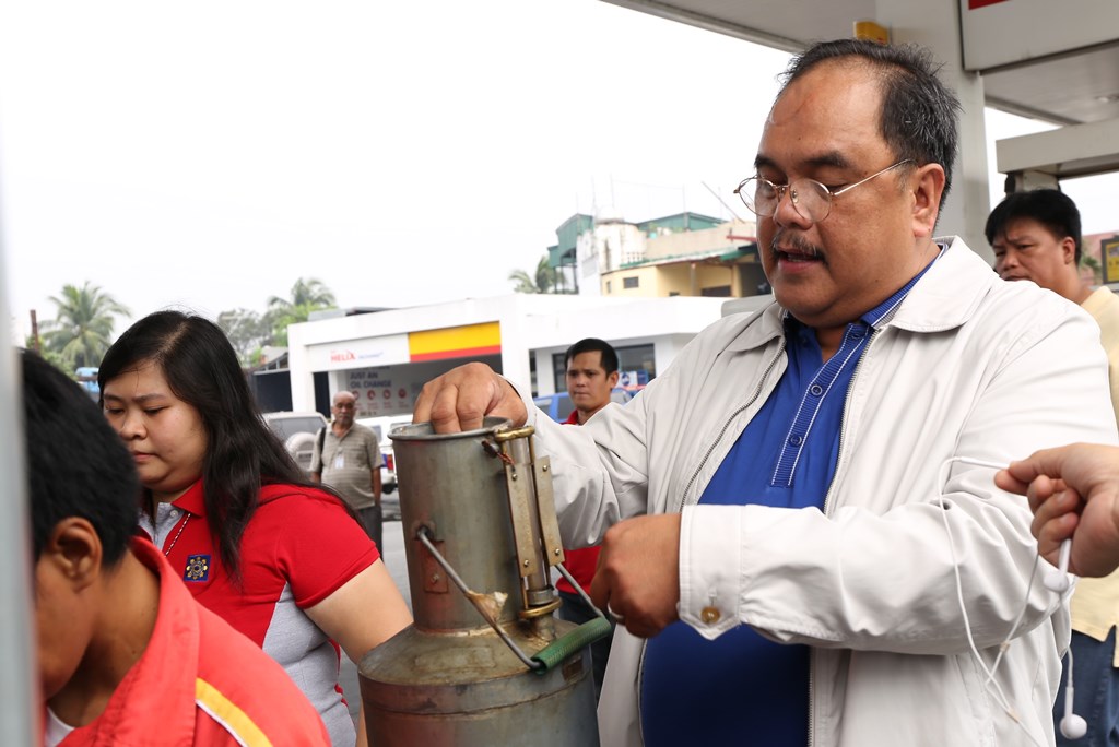 FUEL STANDARD INSPECTION: DOE Usec. Donato D. Marcos inspects a calibrating bucket to check compliance with standards for liquid petroleum products sold by gasoline stations/retail outlets. (PHOTO COURTESY OF DOE)