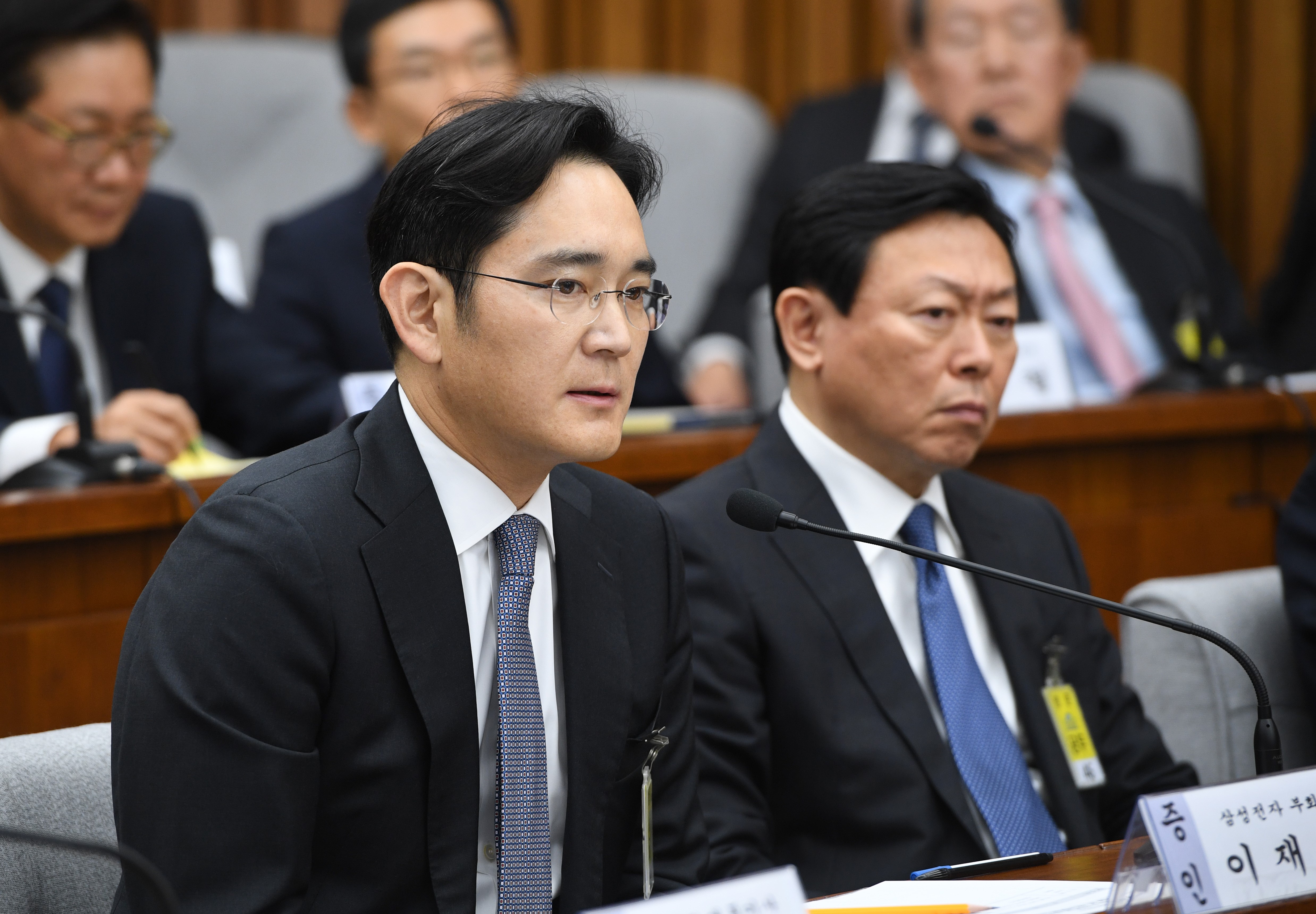 Samsung Group's heir-apparent Lee Jae-Yong (L) answers a question as Lotte Group Chairman Shin Dong-Bin (R) listens to during a parliamentary probe into a scandal engulfing President Park Geun-Hye at the National Assembly in Seoul on December 6, 2016.  The publicity-shy heads of South Korea's largest conglomerates faced their worst nightmare on December 6, as they were publicly grilled about possible corrupt practises before an audience of millions. / AFP PHOTO / POOL / JUNG YEON-JE