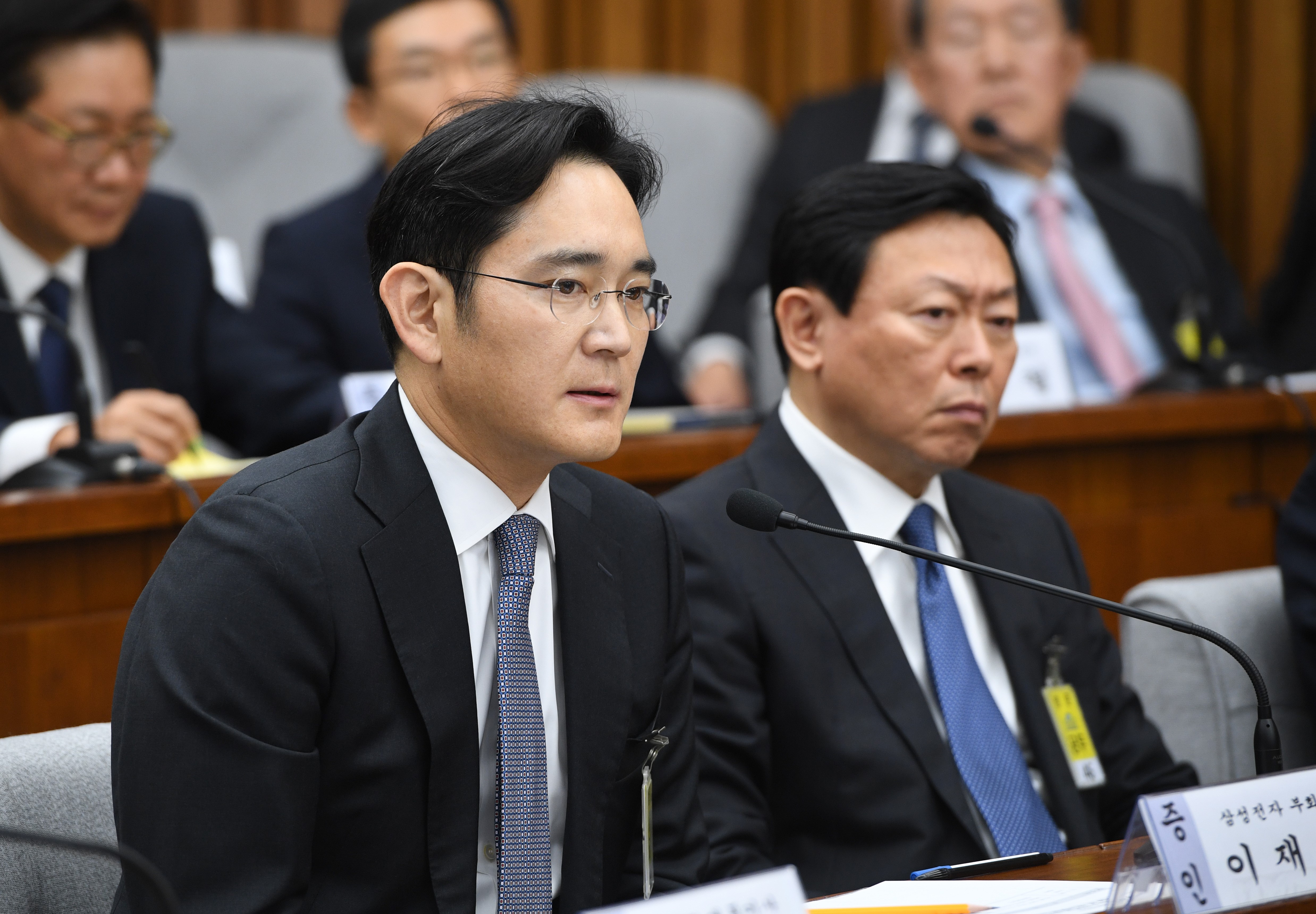 Samsung Group's heir-apparent Lee Jae-Yong (L) answers a question as Lotte Group Chairman Shin Dong-Bin (R) listens to during a parliamentary probe into a scandal engulfing President Park Geun-Hye at the National Assembly in Seoul on December 6, 2016. The publicity-shy heads of South Korea's largest conglomerates faced their worst nightmare on December 6, as they were publicly grilled about possible corrupt practises before an audience of millions. / AFP PHOTO / POOL / JUNG YEON-JE