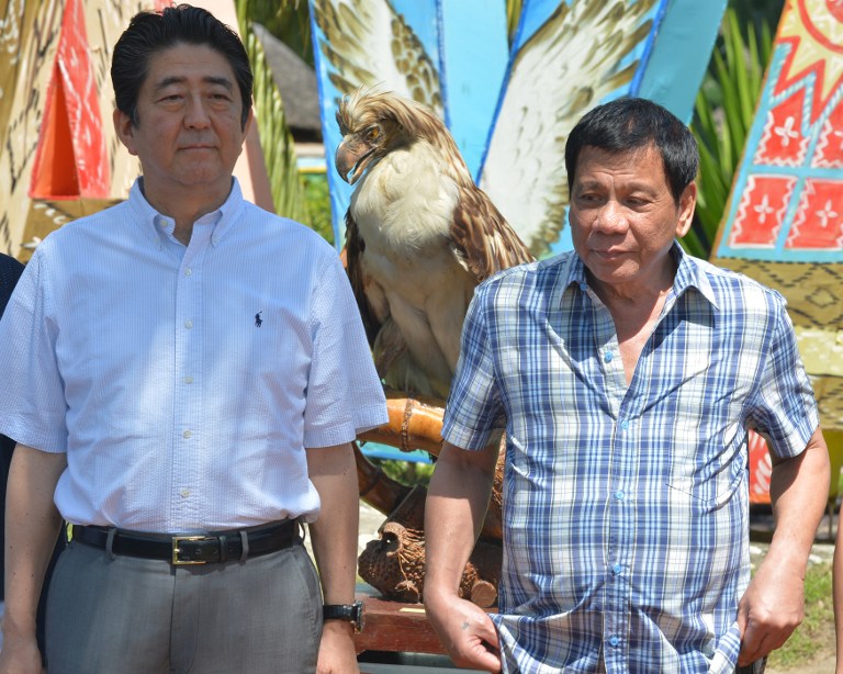 Japanese Prime Minister Shinzo Abe (L) and Philippine President Rodrigo Duterte stand next to a stuffed Philippine eagle during the naming of eagle ceremony in Davao city in southern island of Mindnao on January 13, 2017. Abe arrived in the Philippines on January 12, becoming the first foreign leader to visit since President Rodrigo Duterte took office last year. / AFP PHOTO / TED ALJIBE