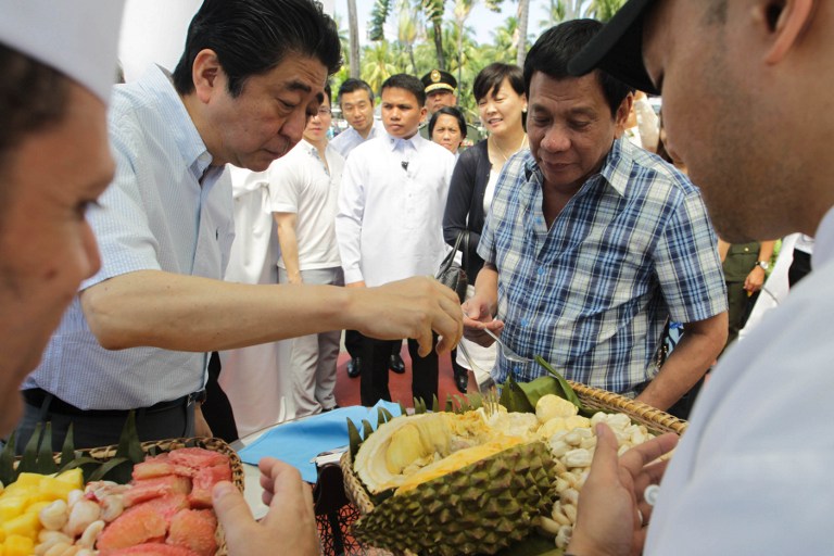 In this photograph released by the Presidential Office on January 13, 2017, Japanese Prime Minister Shinzo Abe (L) eats durian fruit with Philippine President Rodrigo Duterte (R) after attending various events in Davao City on the southern island of Mindanao. Duterte gave visiting Abe a cozy taste of his southern home town on January 13, shunning stiff ceremonies for breakfast in his house as well as durian diplomacy. / AFP PHOTO / Presidential Office / SIMEON CELI