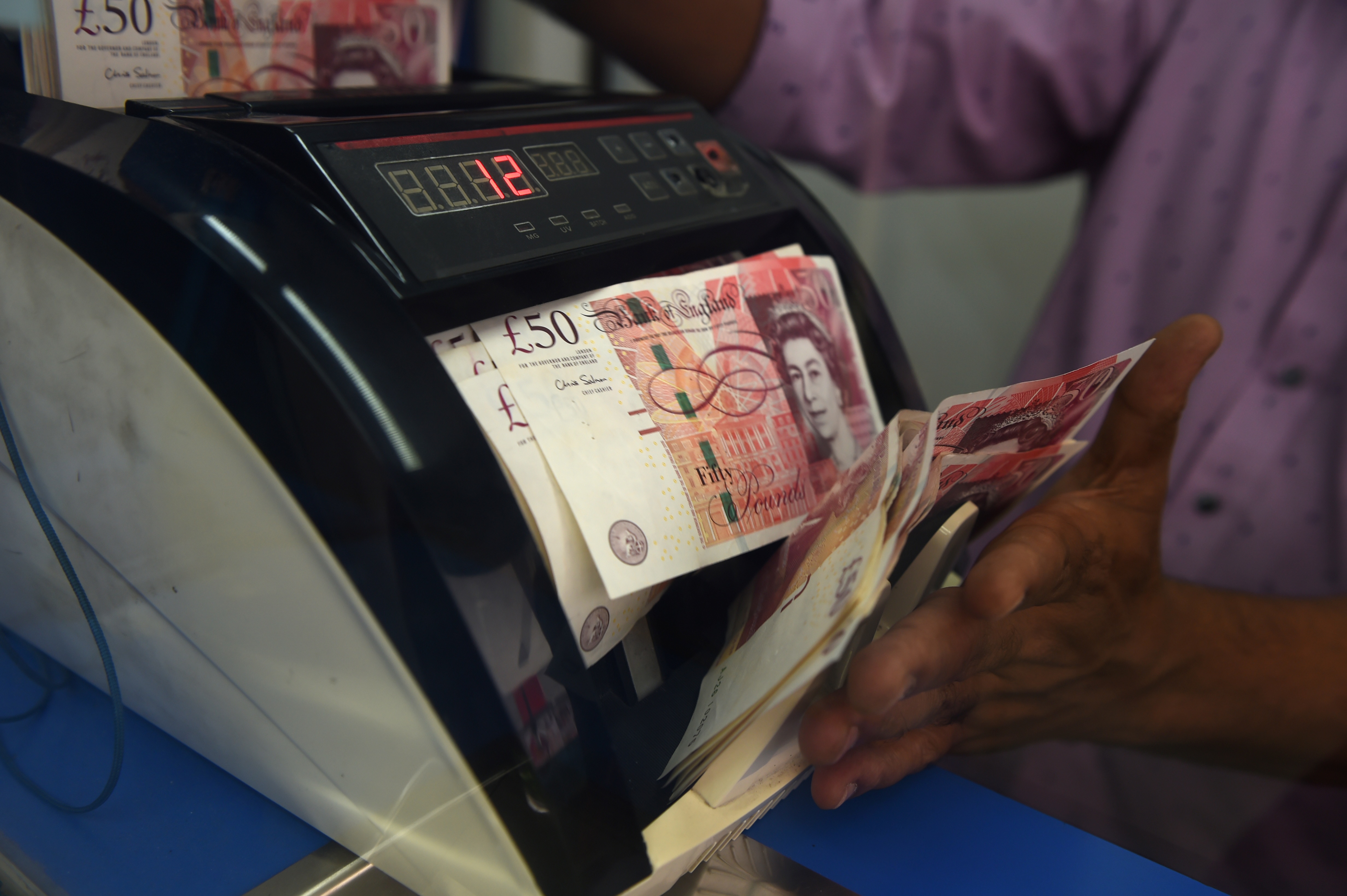 A money changer drops British pound notes into a counting machine at a currency exchange in Kuala Lumpur on January 16, 2017.  The pound struggled at 32-year lows against the dollar in Asia on January 16 after reports said British Prime Minister Theresa May was ready to take the country out of the European Union in a so-called "hard Brexit". / AFP PHOTO / MOHD RASFAN