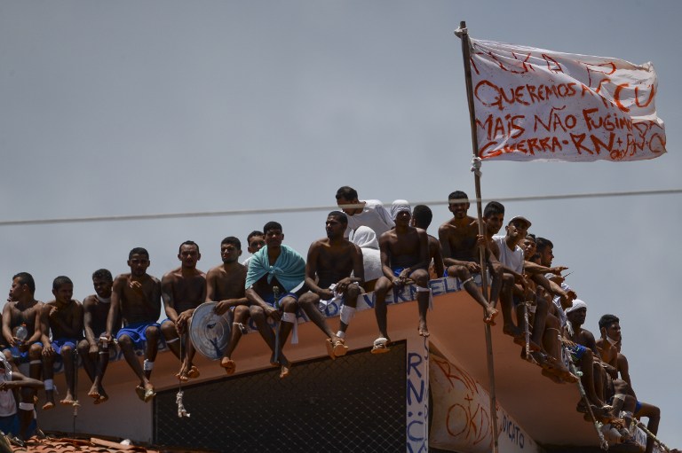 Inmates stand on the prison roof waving a flag that reads "We want peace but don't run away from war" during a rebellion in Alcacuz Penitentiary Center near Natal, Rio Grande do Norte state, northeastern Brazil on January 16, 2017. The latest in a string of brutal prison massacres involving suspected gang members in Brazil has killed 26 inmates, most of whom were beheaded. The bloodbath erupted Saturday night in the overcrowded Alcacuz prison in the northeastern state of Rio Grande do Norte. Similar violence at other jails in Brazil left around 100 inmates dead in early January.  / AFP PHOTO / ANDRESSA ANHOLETE