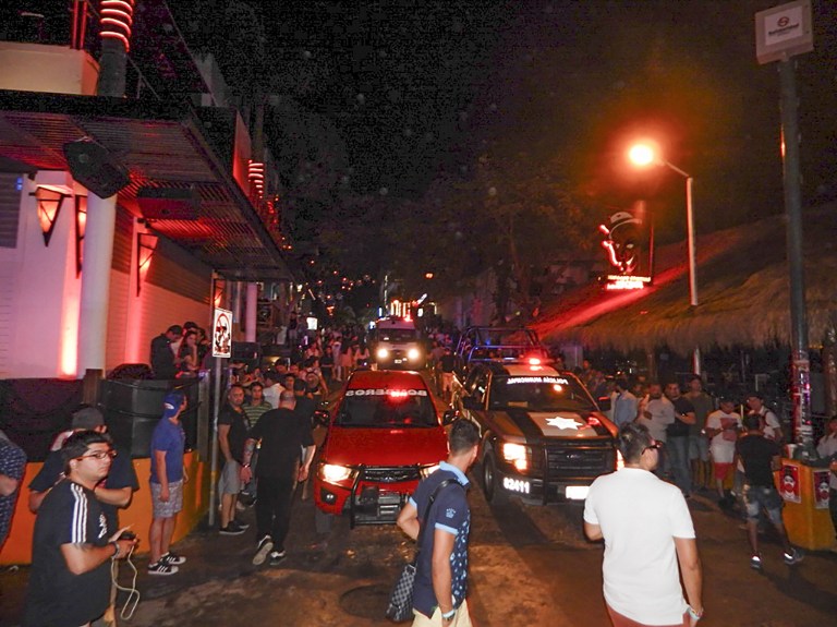 People remain in the street outside the Blue Parrot nightclub as firefighters and police agents patrol the area in Playa del Carmen, Quintana Roo state, Mexico where 5 people were killed, three of them foreigners, during a music festival on January 16, 2017. A shooting erupted at an electronic music festival in the Mexican resort of Playa del Carmen early Monday, leaving at least five people dead and sparking a stampede, the mayor said. Fifteen people were injured, some in the stampede, after at least one shooter opened fire before dawn at the Blue Parrot nightclub during the BPM festival. / AFP PHOTO / VICTOR VARGAS / MAXIMUM QUALITY AVAILABLE
