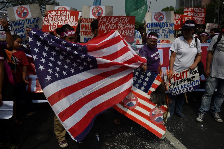 Activists burn a mock US flag (R) with President-elect Donald Trump's portrait and a real one (L) during a rally in front of the US embassy in Manila on January 20, 2017, ahead of Trump's presidential inauguration Hundreds of Filipinos converged on the US embassy to denounce Trump ahead of his inauguration as president of the United States, accusing him of sexism, racism and xenophobia. / AFP PHOTO / TED ALJIBE