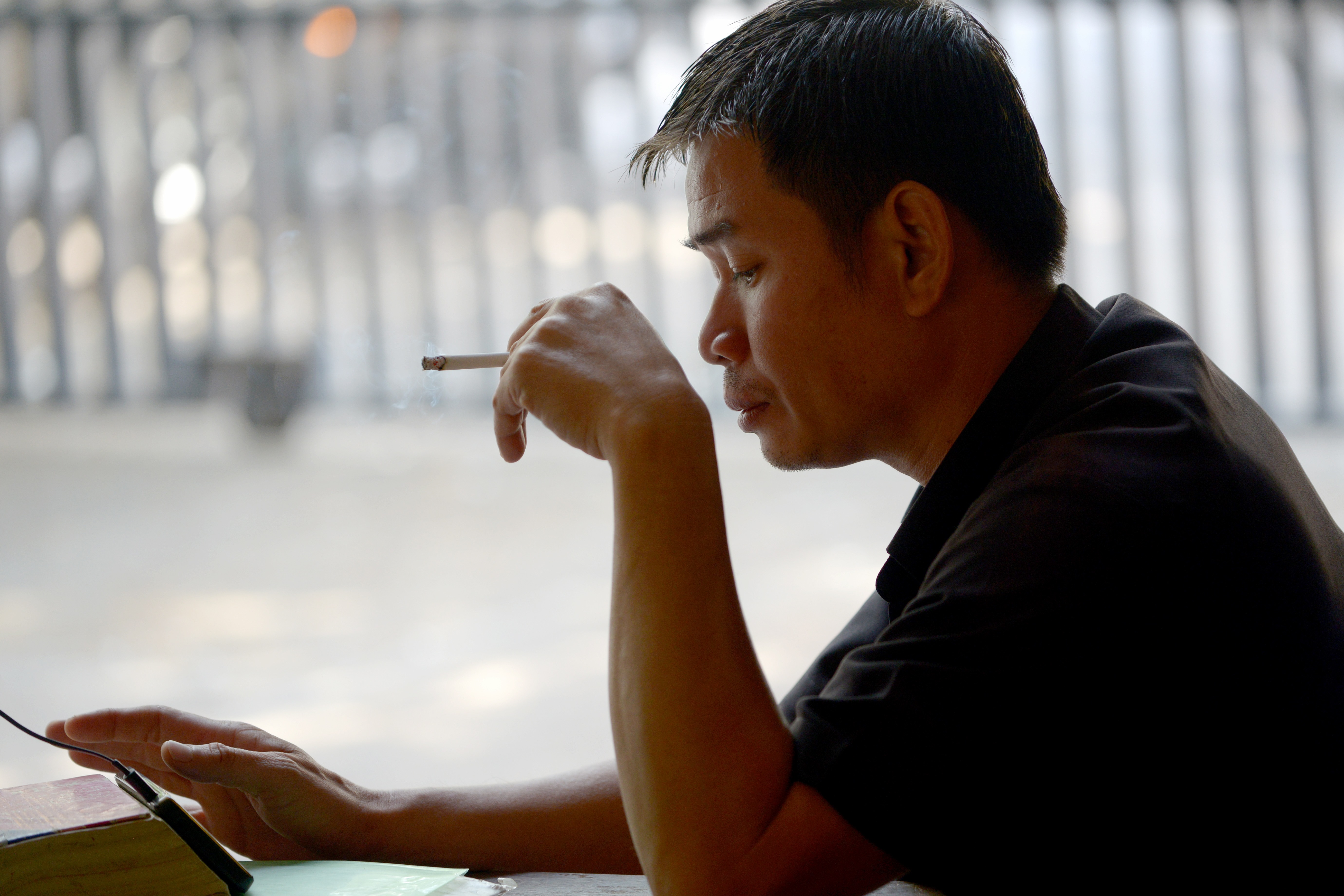 A Cambodian man smokes a cigarette as he plays with his smartphone in Phnom Penh on January 31, 2017. Smoking cost the world economy more than 1.4 trillion USD in 2012, and sucked up a twentieth of health care spending, a study said on January 31. / AFP PHOTO / TANG CHHIN SOTHY