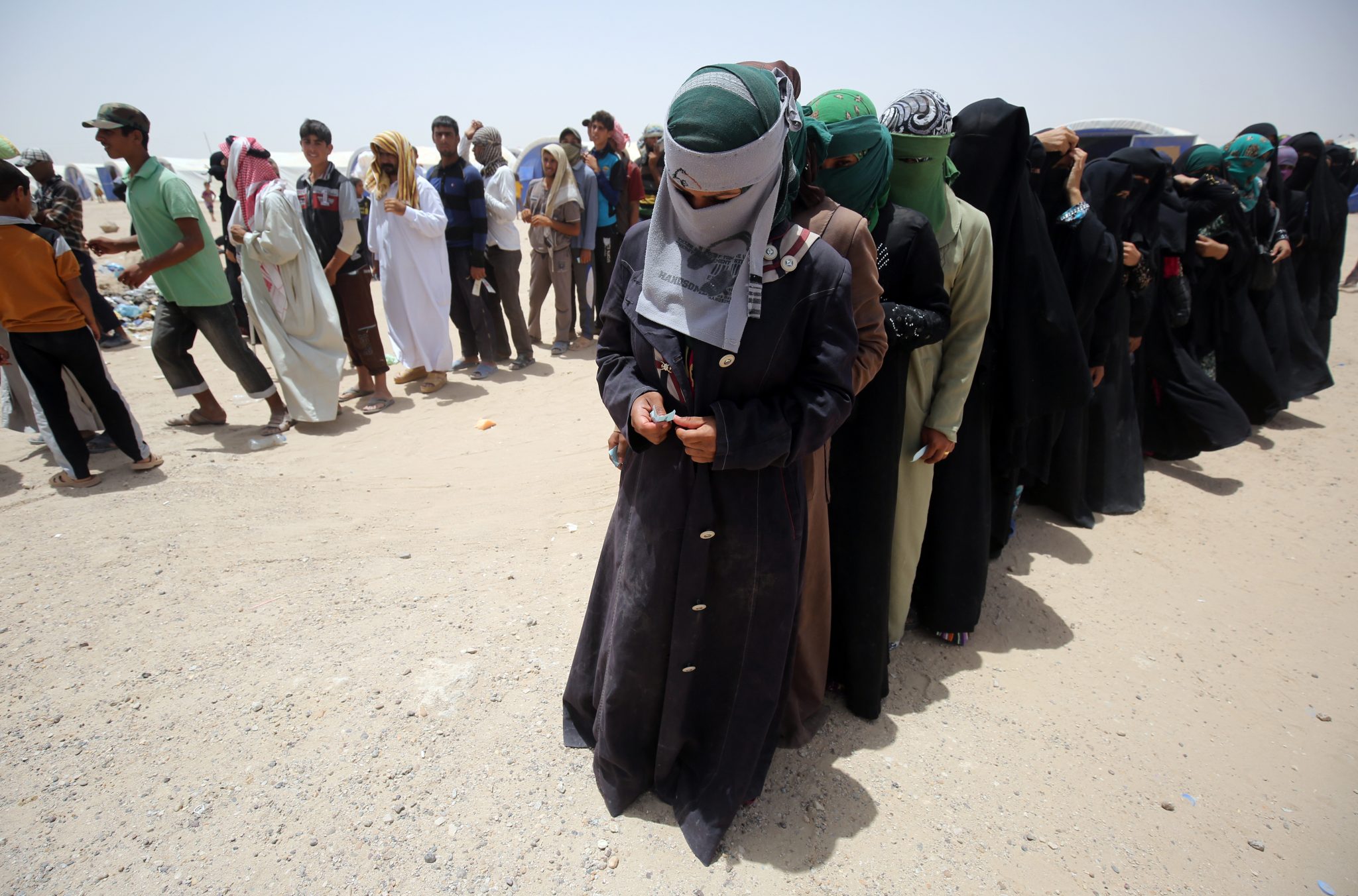 Iraqis displaced from the city of Fallujah queue up to collect aid distributed by the Norwegian Refugee Council at a newly opened camp where they are taking shelter in Amriyat al-Fallujah on June 27, 2016, south of Fallujah. Iraqi forces on June 26 wrapped up operations in Fallujah and declared the area free of jihadists from the Islamic State (IS) group after a month-long operation. The government said the destruction caused by the fighting was limited and vowed to do its utmost to allow the tens of thousands of displaced civilians to return to their homes.  / AFP PHOTO / AHMAD AL-RUBAYE