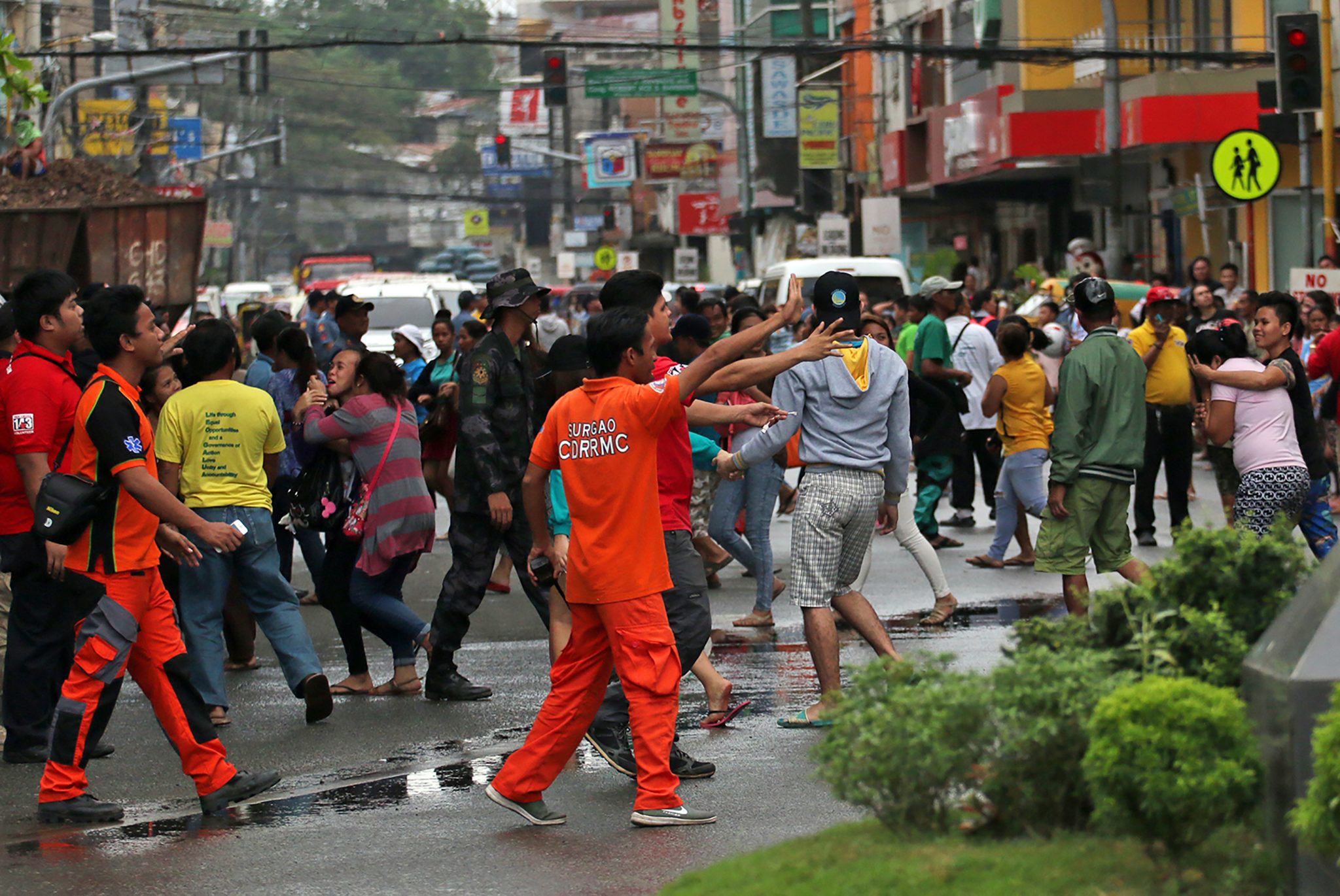 Residents run to a main road as rescuers (in orange) give instructions as strong after-shocks struck, prior to the arrival of Philippine President Rodrigo Duterte in Surigao City, in southern island of Mindanao on February 12, 2017, days after a 6.5-magnitude earthquake hit the city. Duterte flew to the region on February 12, to inspect the response effort, which officials said has shifted to relief and rehabilitation after the last of the dead and injured were pulled from the rubble. / AFP PHOTO / ERWIN MASCARINAS