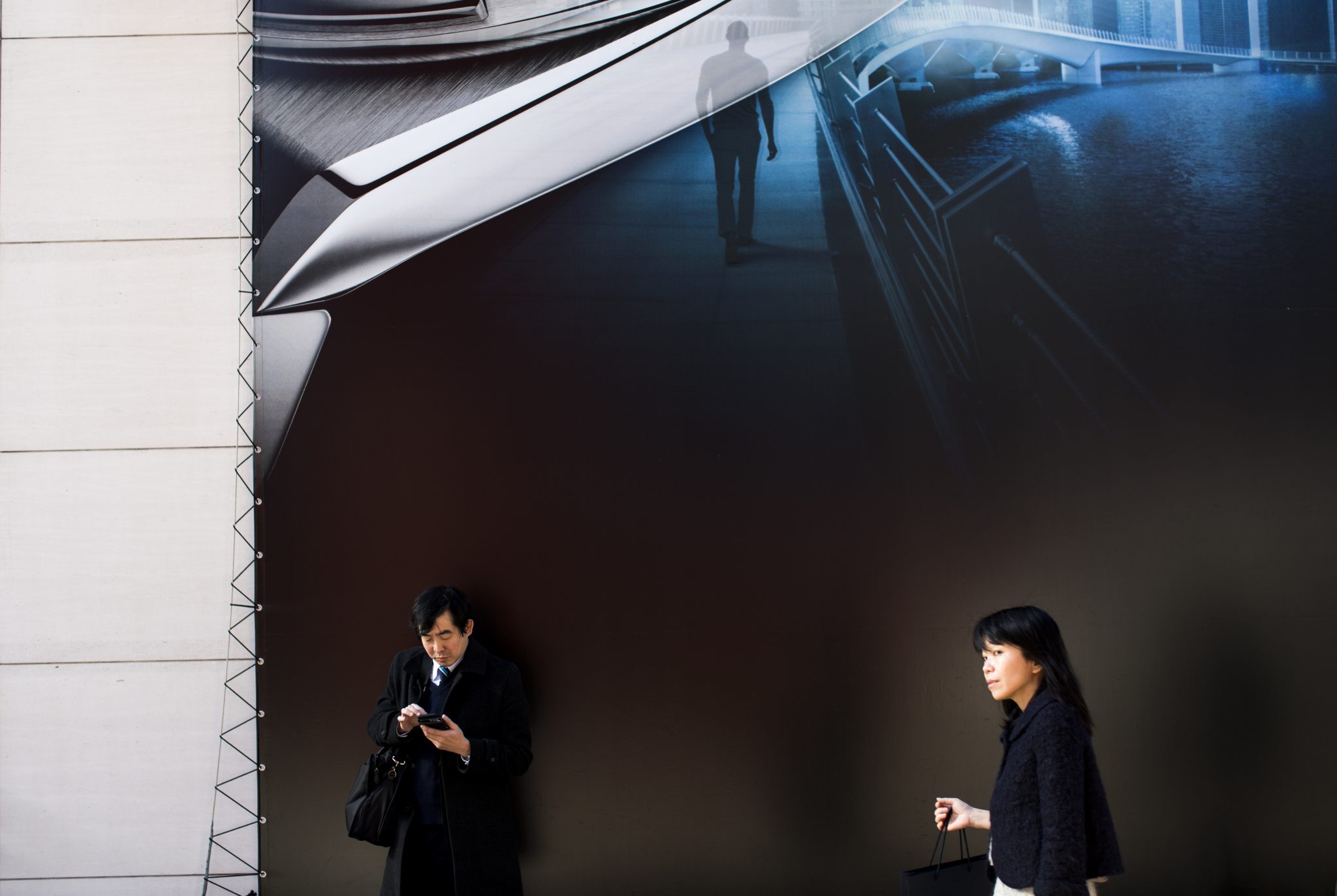 A woman walks past advertising as a man checks his mobile phone in the Ginza shopping district in Tokyo on February 13, 2017. Japan's economy expanded 1.0 percent in 2016 as a bump in exports and capital investment offset weak spending at home, data showed on February 13, 2017, although it was unlikely to erase concerns about Tokyo's faltering war on deflation. / AFP PHOTO / Behrouz MEHRI