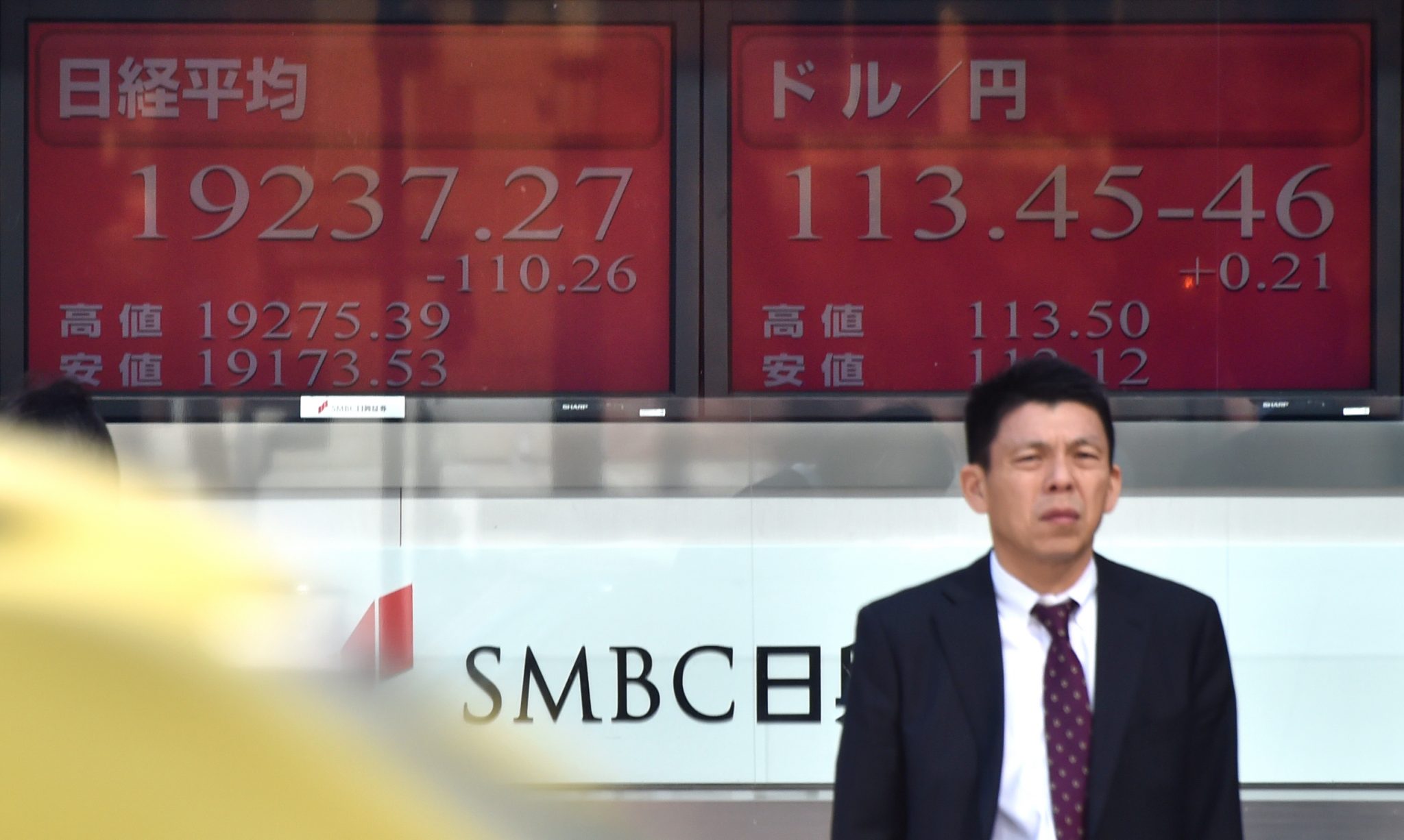 A pedestrian stands in front of an electric quotation board flashing the Nikkei key index of the Tokyo Stock Exchange (L) and the current exchange rate of the Japanese yen against the US dollar (R) in Tokyo on February 17, 2017. Sharp jumped 2.17 percent to 329 yen after the company slashed its net loss estimate by more than a quarter to 27 billion yen ($238 million) for the year to March, citing lower materials costs. / AFP PHOTO / KAZUHIRO NOGI