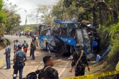 Police and soldiers stand guard next to a tourist bus which hit an electric post in Tanay town, Rizal province, east of Manila on February 20, 2017. Local media reports said that at least 10 students were killed and more than 20 others injured after the bus hit the post when the driver lost control of the vehicle when the brakes failed. / AFP PHOTO / STR