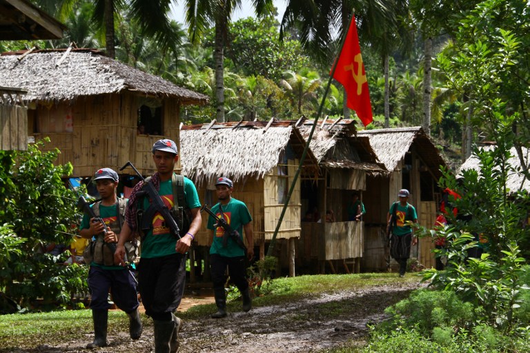 In this photo taken on December 26, 2014, members of the communists' armed wing, the New People's Army (NPA), walk past a hammer and sickle flag displayed in a village as they mark the 46th anniversary of its founding, on the southern island of Mindanao. The Philippine government and communist rebels said on December 26 that formal negotiations to end a lengthy insurgency could restart shortly, though the rebels' armed wing announced it was beefing up its guerilla campaign. AFP PHOTO / AFP PHOTO / STR