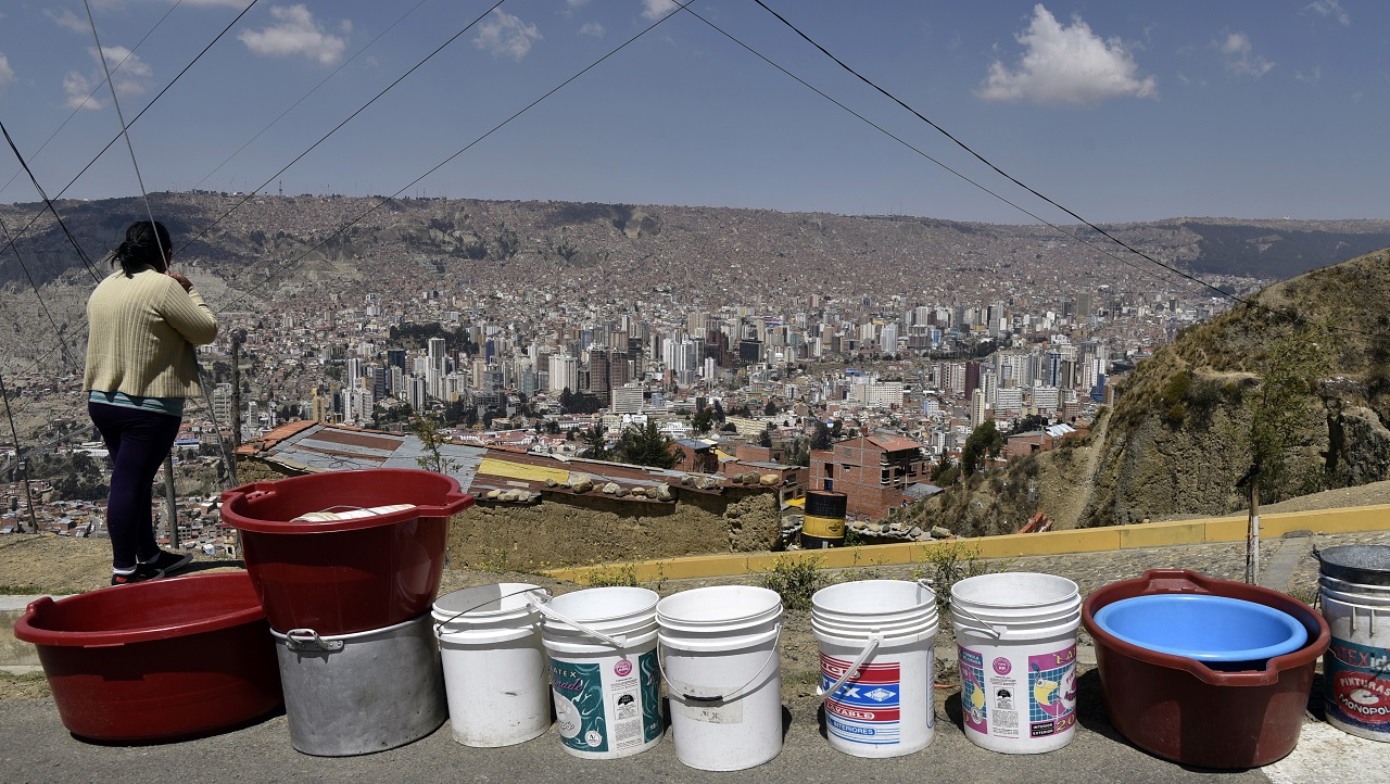 A woman remains next to a line of empty buckets and containers prepared by the inhabitants of a neighbourhood to wait for a water supply tanker, in La Paz on November 23, 2016. Bolivia suffers its worst drought in 25 years. The shortages have sparked protests in various areas, including rural districts whose crops depend on irrigation. / AFP PHOTO / AIZAR RALDES