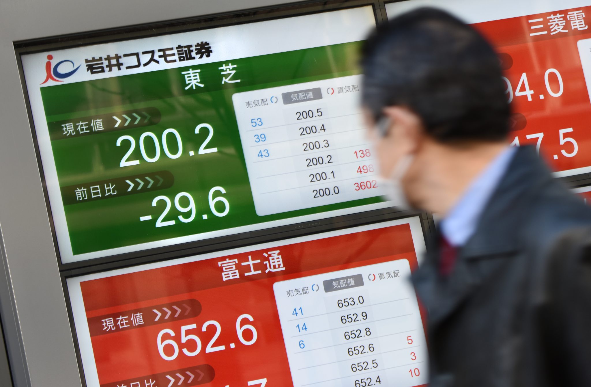 A businessman looks at an electric quotation board flashing the share price of Japan's Toshiba (top/L) in front of a securities company in Tokyo on February 15, 2017. Toshiba shares tumbled more than 10 percent after the company warning of a 6.2 billion USD writedown in its US nuclear power business, as investors questioned the conglomerate's corporate governance. / AFP PHOTO / TORU YAMANAKA