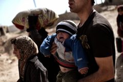 An Iraqi man walks down a road carrying a child as families flee Mosul on February 28, 2017, during an offensive by security forces to retake the western parts of the city from Islamic State (IS) group fighters. / AFP PHOTO / ARIS MESSINIS