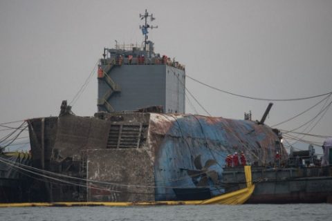 Workers stand before a propellor of the wreck of the Sewol ferry during its the salvage operation off the coast of South Korea's southern island of Jindo on March 24, 2017. South Koreas sunken Sewol ferry emerged from the waters March 23, nearly three years after it went down with the loss of more than 300 lives and dealt a crushing blow to now-ousted president Park Geun-Hye. / AFP PHOTO / AFP PHOTO AND POOL / Ed JONES