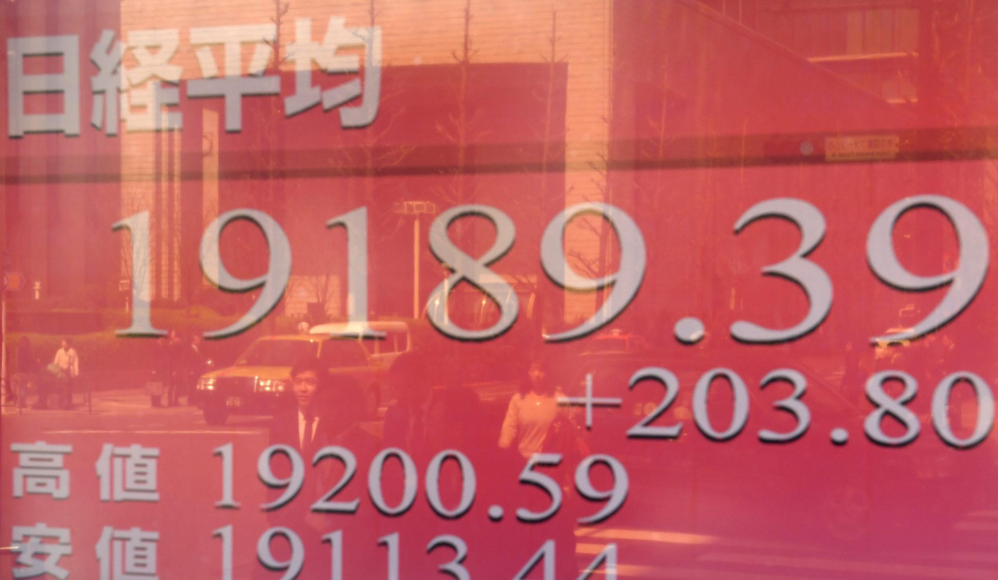 Pedestrians are reflected in a window of a security company with an electronic stock indicator flashing the morning closing rate of the Tokyo stock market in Tokyo on March 28, 2017. The benchmark Nikkei 225 index rose 1.07 percent, or 203.80 points, to 19,189.39 by the break, recovering from the previous day's sharp sell-off with dealers still hopeful Donald Trump can push through his planned tax and spending agenda despite last week's healthcare bill collapse. / AFP PHOTO / Toshifumi KITAMURA