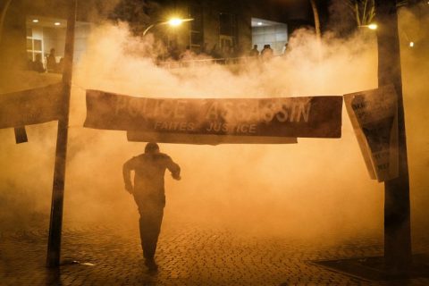 A man runs away from tear gas launched by riot police next to a banner reading "Police murderer, Do justice" during a protest in front of the police headquarters in the 19th arrondissement of Paris on March 28, 2017, following the death of a Chinese national during a police intervention on March 26. China on march 28 called on France to protect its citizens after police in Paris killed a Chinese father of five, sparking violent protests in which 35 people were arrested. / AFP PHOTO / GEOFFROY VAN DER HASSELT