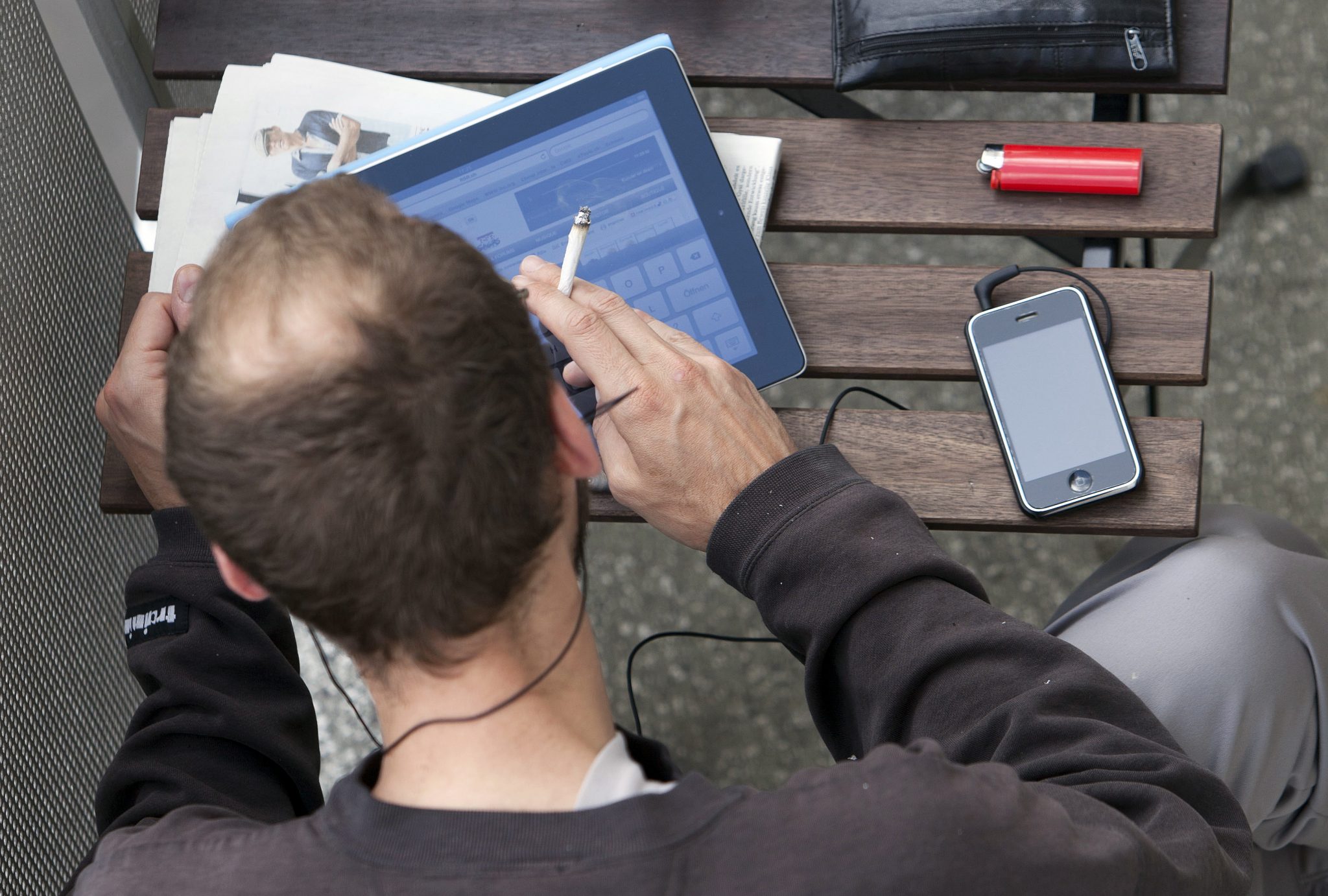 A man sitting on a balcony surfs the web on an iPad while listening to music on his iPhone in Berlin on June 23, 2011. AFP PHOTO / DAVID GANNON / AFP PHOTO / DAVID GANNON