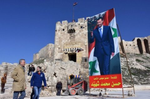 United Nations (UN) High Commissioner for Refugees Filippo Grandi (L) walks past a poster of Syrian President Bashar al-Assad as he visits the old city of the northern Syrian city of Aleppo on February 1, 2017. / AFP PHOTO / George OURFALIAN