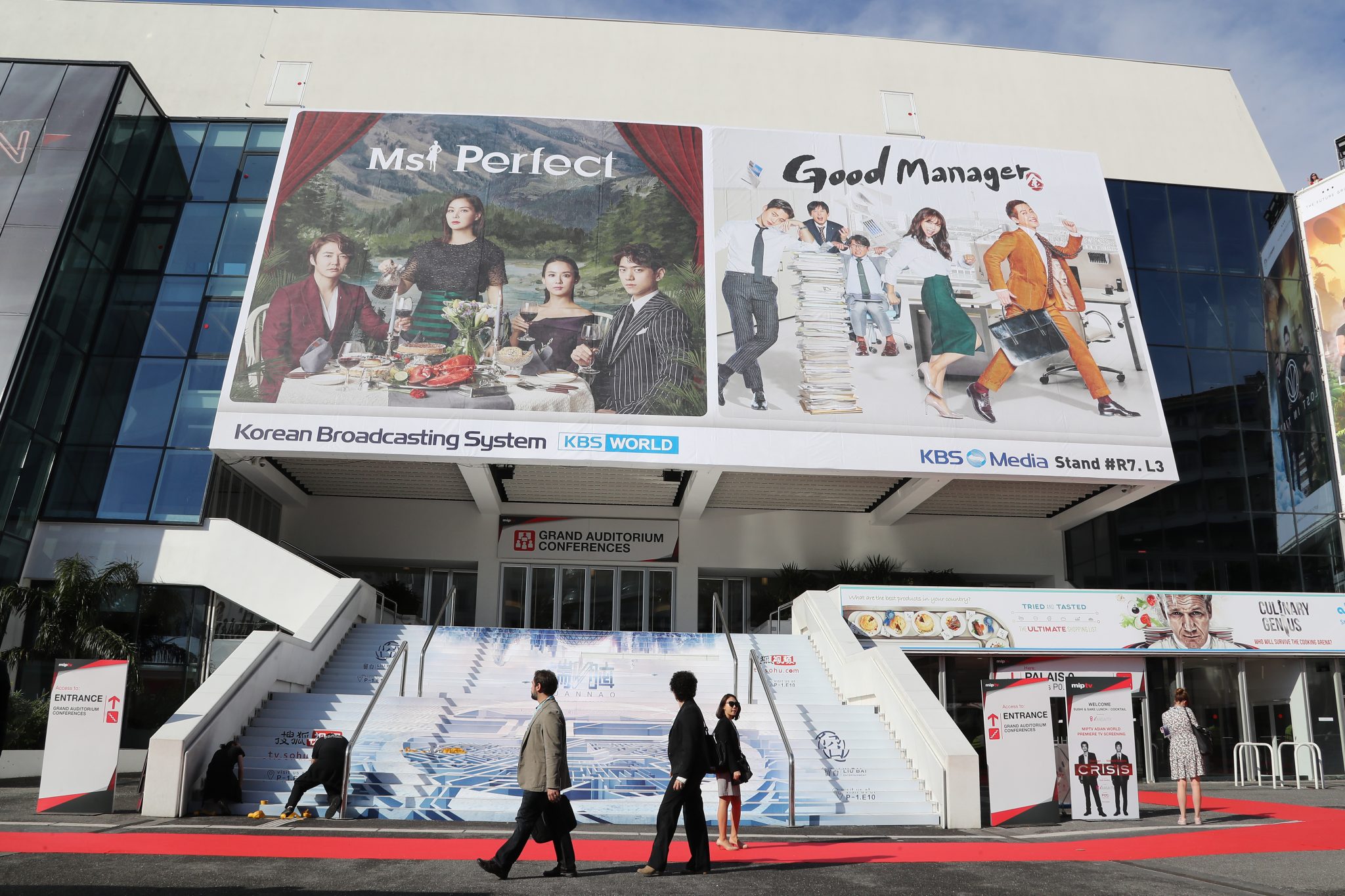 People walk past  billboards for the series "Ms Perfect" and "Good Manager" outside the Palais des Festivals during the MIPTV event on April 3, 2017 in Cannes, southeastern France. / AFP PHOTO / VALERY HACHE