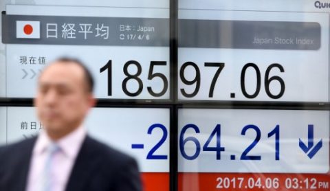A businessman walks past a stock quotation board flashing the Nikkei 225 key index of the Tokyo Stock Exchange in front of a securities company in Tokyo on April 6, 2017. Tokyo stocks fell to a four-month low on April 6 after Federal Reserve minutes suggested the US central bank was considering steps that could result in a further tightening of monetary policy. / AFP PHOTO / Toru YAMANAKA
