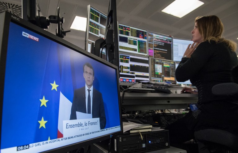 A television screen displays an image of France's President-elect Emmanuel Macron, as traders works on the trading floor of ETX Capital in London on May 8, 2017, following the result of France's presidential election. The Paris stock market rose slightly at the open Monday after the expected French presidential election win for Emmanuel Macron. Macron won a resounding victory in the French presidential election but the focus will shift immediately Monday to whether he can govern the country without the support of a traditional party. / AFP PHOTO / CHRIS J RATCLIFFE