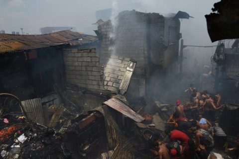 Residents jostle for position as they scavenge for recyclable materials to be sold later, amidst smoke and smouldering debris after a fire hit an informal settlers area near a container port in Manila on May 9, 2017. Local media reported a teenage boy died and 30 houses were burnt in the incident. / AFP PHOTO / TED ALJIBE