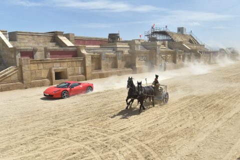 Ferrari driver Fabio Barone and his Ferrari 458 Italia competes against a Roman chariot drawn by two horses on "Ben Hur" movie set at Cinecitta World amusement park on May 11, 2017 in Castel Romano near Rome. / AFP PHOTO / Andreas SOLARO