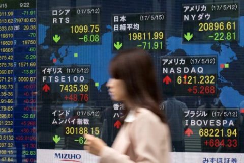A woman walks past a quotation board displaying numbers of the world stock markets in front of a securities company in Tokyo on May 15, 2017. Tokyo stocks opened lower on May 15 with a stronger yen pressuring exporter shares as geopolitical risks linger with North Korea's continued missile tests. / AFP PHOTO / Kazuhiro NOGI
