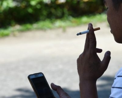 A man smokes while browsing his mobille phone along a walkway in Manila on May 19, 2017. Philippine President Rodrigo Duterte imposed a strict smoking ban, barring the use of tobacco outside in restrictive "smoking areas" and ordering police and local governments to enforce the rules. / AFP PHOTO / TED ALJIBE