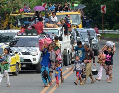 A family carrying their belongings walks in front of other residents in vehicles as they flee from Marawi on the southern island of Mindanao on May 26, 2017, as fighting between Islamist militants and government forces continues. Philippine security forces bombed residential areas in a southern city on May 25 as they battled Islamist militants who were holding hostages and reported to have murdered at least 11 civilians. / AFP PHOTO / Ted ALJIBE