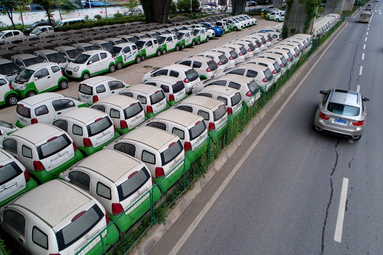 FILE PHOTO: This photo taken on May 22, 2017 shows a car passing new electric vehicles parked in a parking lot under a viaduct in Wuhan, central China's Hubei province. / AFP PHOTO / STR / China OUT
